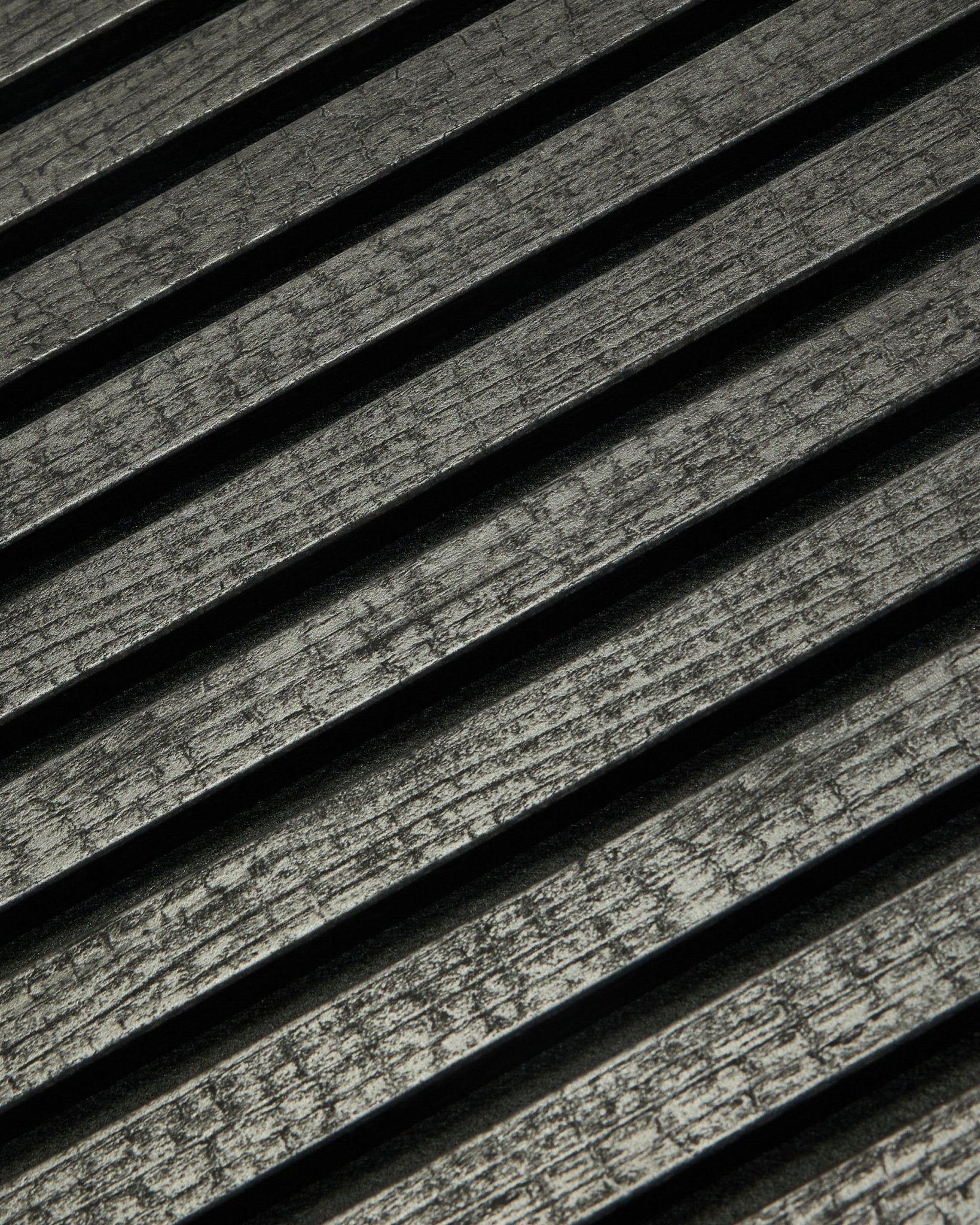 Närbild av WoodUpp Rebel Akupanel i Charcoal (240x60 cm) som visar black, räfflade akustiklameller placerade diagonalt för förbättrad ljudabsorption.