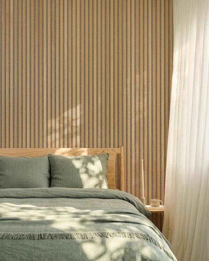 Minimalistiskt nordiskt sovrum med en WoodUpp Akupanel vägg i ek Akustikpanel, salviagröna sängkläder, sängram i trä och skira vita gardiner.