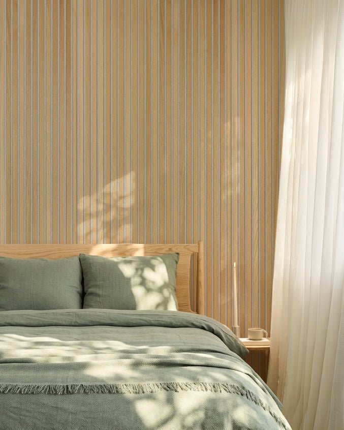 Minimalistiskt nordiskt sovrum med sängkläder i salviagrönt och en WoodUpp Classic Oak Akupanel akustisk ribbvägg; solljuset skapar mjuka skuggor på sängen.