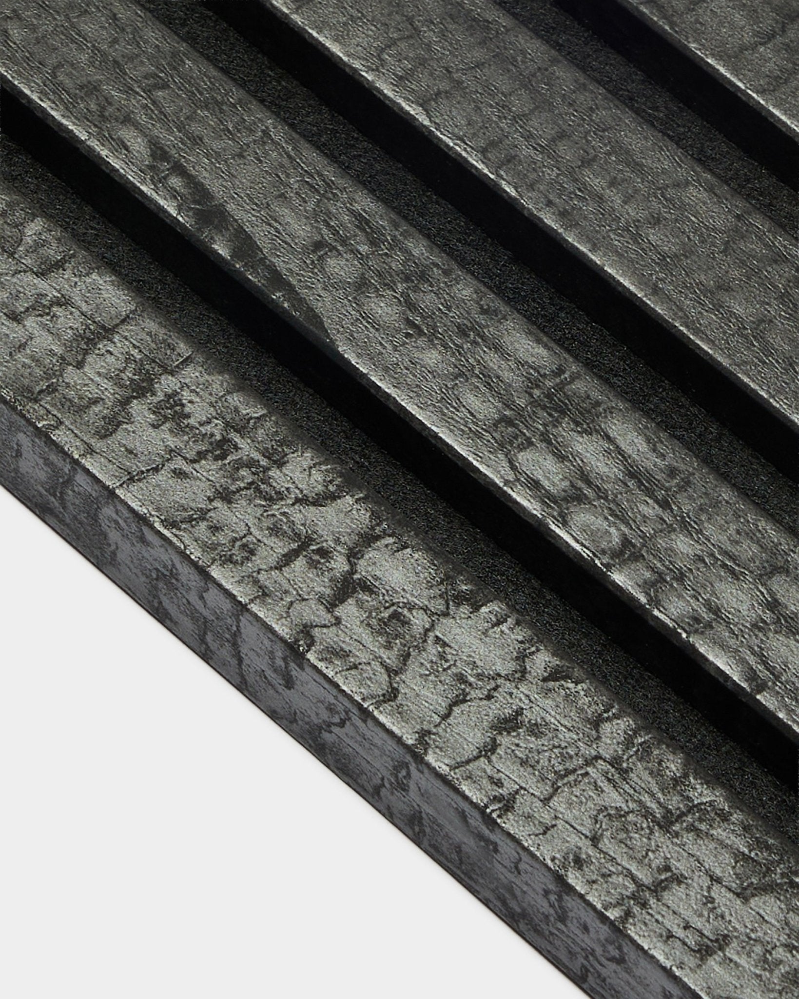 WoodUpp Akupanel ändlamell i Charcoal (2,2 cm), med diagonala, texturerade akustikpaneler i trä med en bränd black-finish för väggmontering.