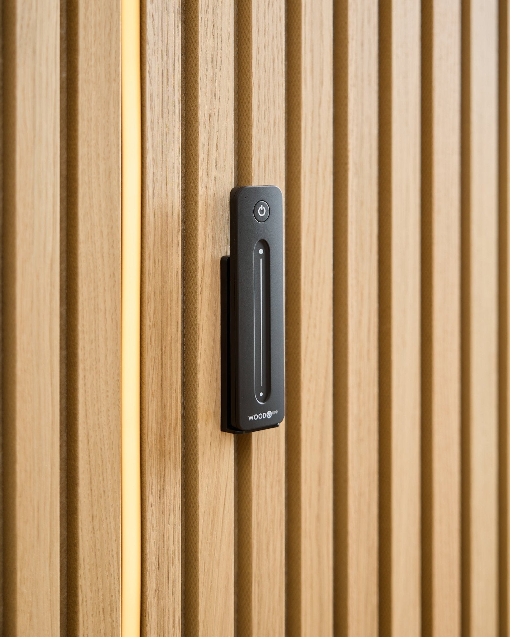 En WoodUpp Lumi | Remote / LED Striplight är monterad på en ljus trä-Akustikpanel, med en gul kabel synlig bakom träribborna.