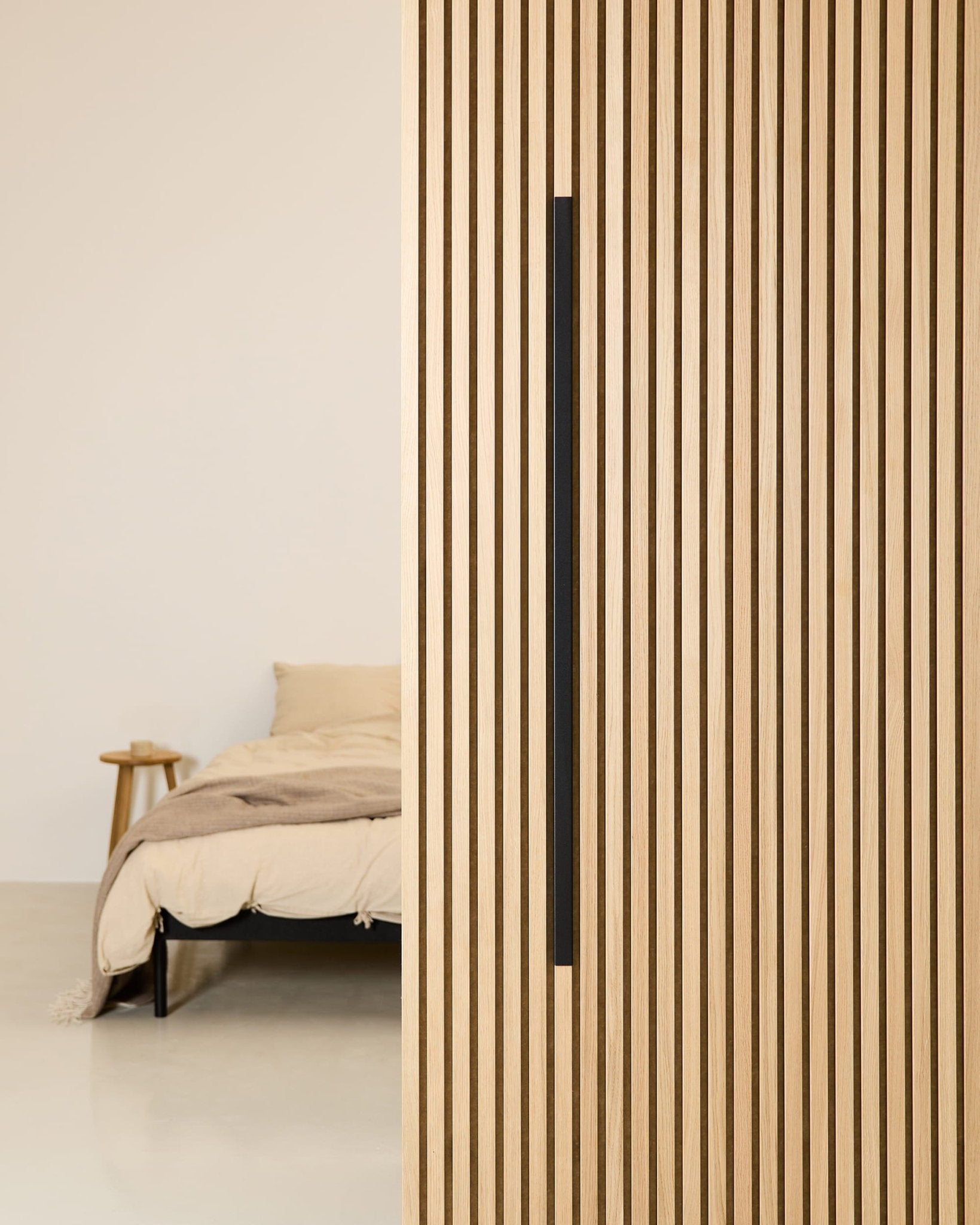 Ett minimalistiskt sovrum med en beige säng, ett sidobord i trä och en akustikpanel av typen WoodUpp Akupanel Black Aluminum 120 cm monterad på väggen.
