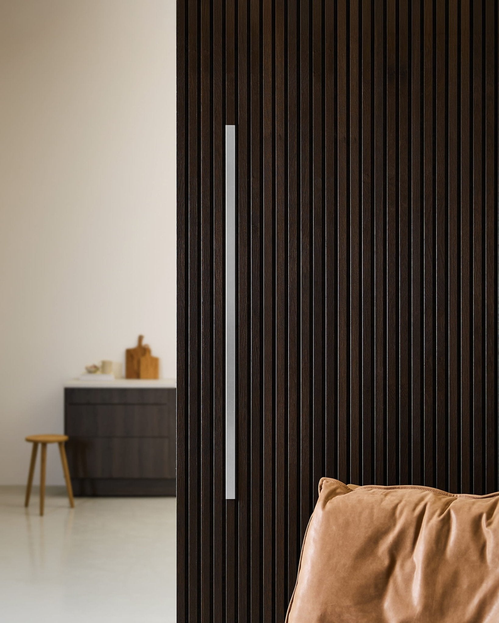 Akupanel-dörr i mörkt trä med WoodUpp Liva Cover, 120 cm långt stålhandtag, dekorlist, läderdyna och ett minimalistiskt nordiskt kök med pall.
