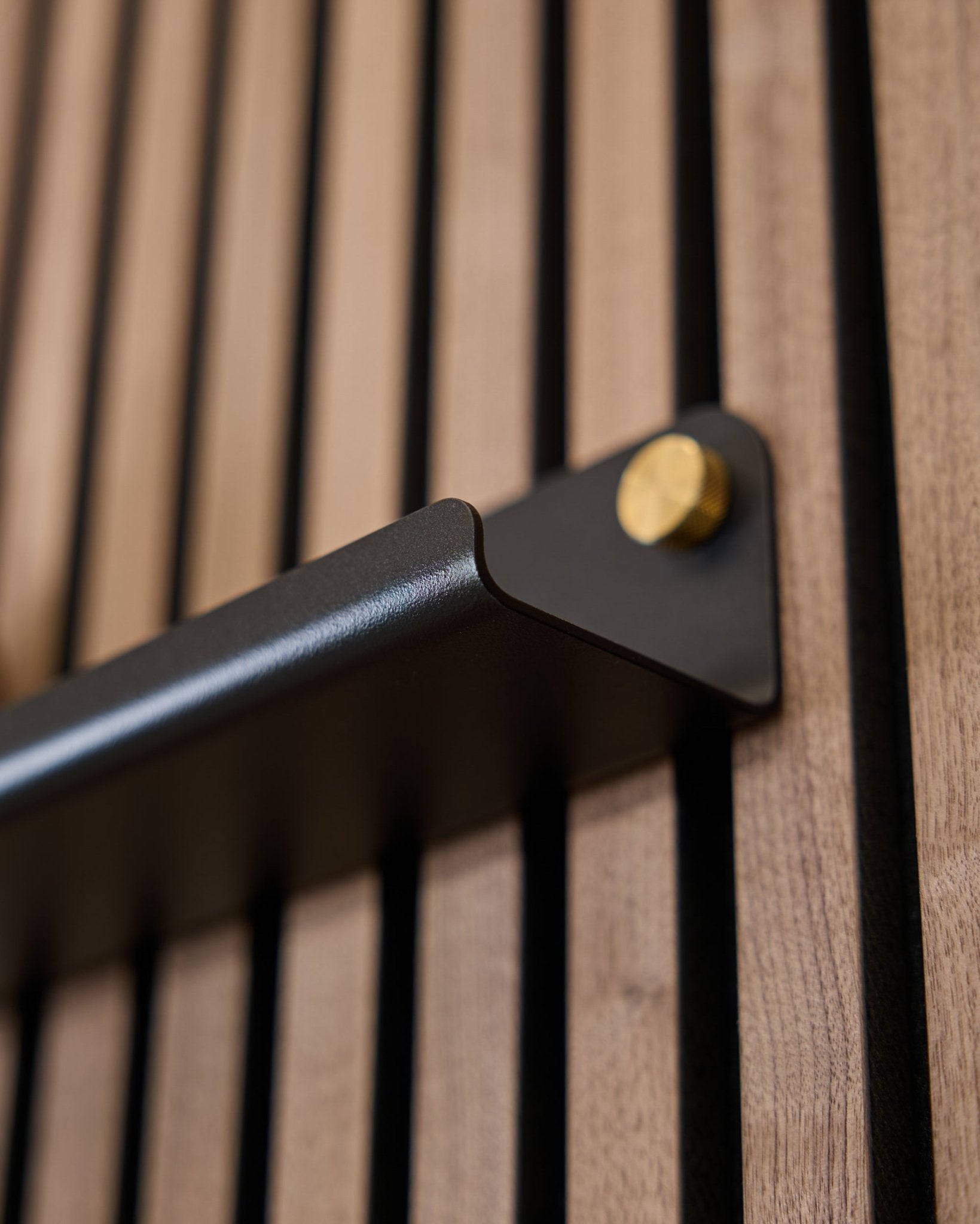 Närbild av Norr | smal hylla (75,9 cm) från WoodUpp i black, med ett steel handtag med guldfärgade bultar och en vertikalt räfflad akustisk yta.