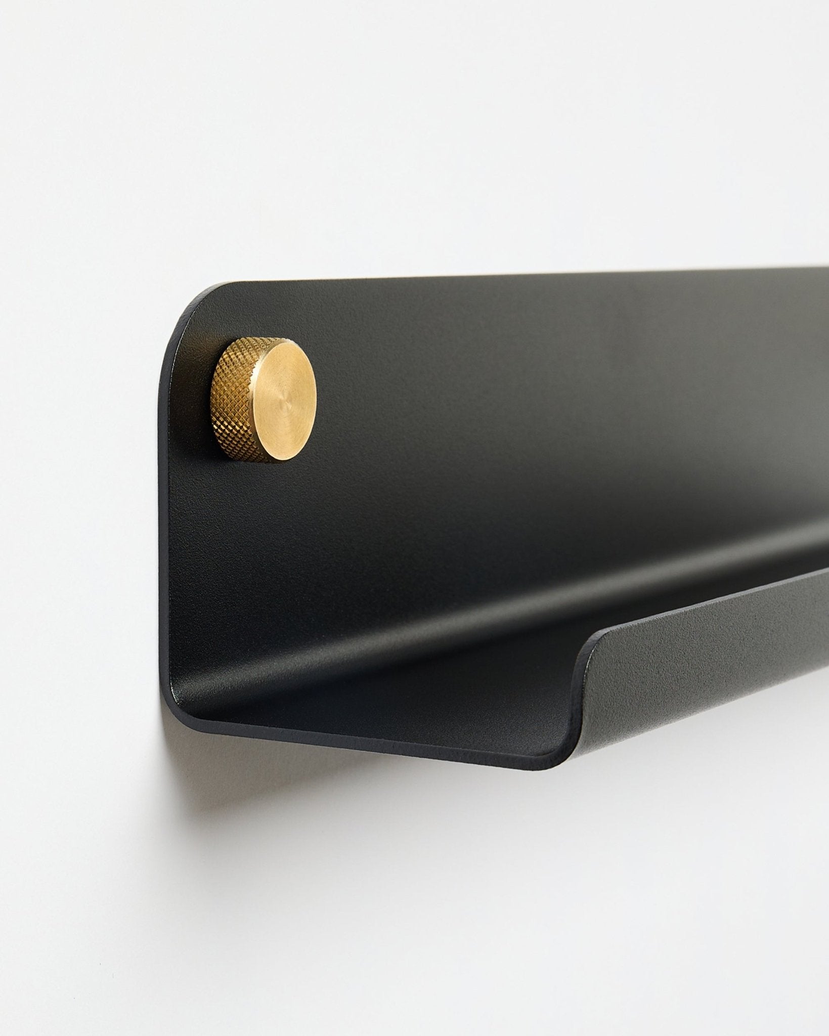 Norr | Narrow Shelf i black (115,9 cm) med en enkel gyllene knopp till vänster, från WoodUpp, monterad på en enkel vit vägg.