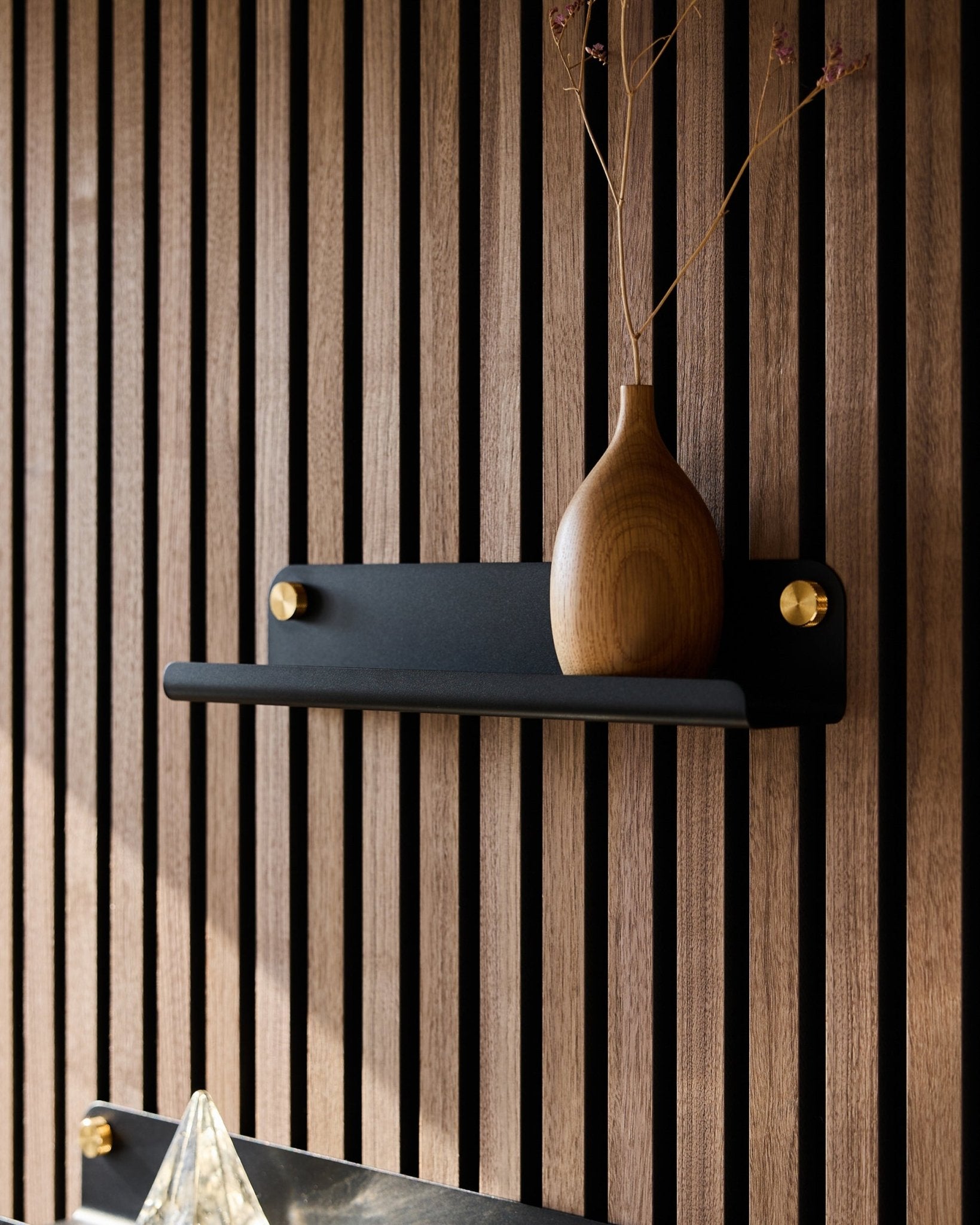 En trävas med torkade grenar på en black WoodUpp Norr smal hylla (35,9 cm), placerad framför en vertical akustisk ribbväggspanel i nordisk stil.