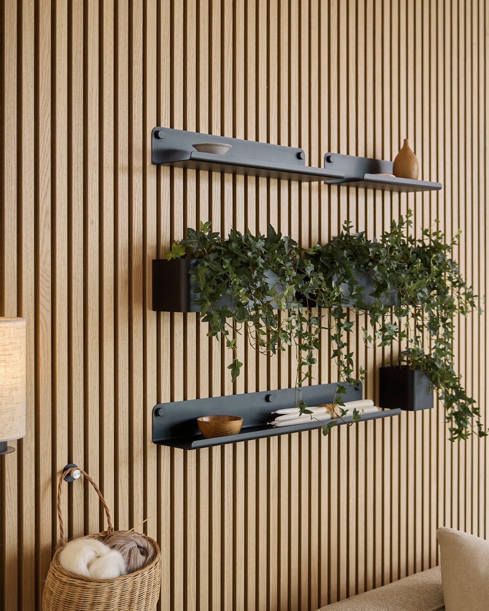 Tre black Norr | Plant Box hyllor från WoodUpp med dekoration och en växt är monterade ovanför en flätad garnkorg, mot en grön akustisk ribbväggspanel.