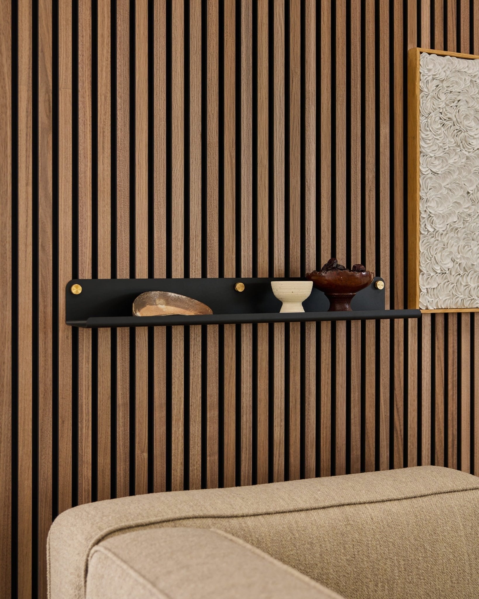 Black WoodUpp Norr bred hylla (75,9 cm) med dekoration ovanför en beige soffa, monterad på en modern akustisk väggpanel av trä med lameller.