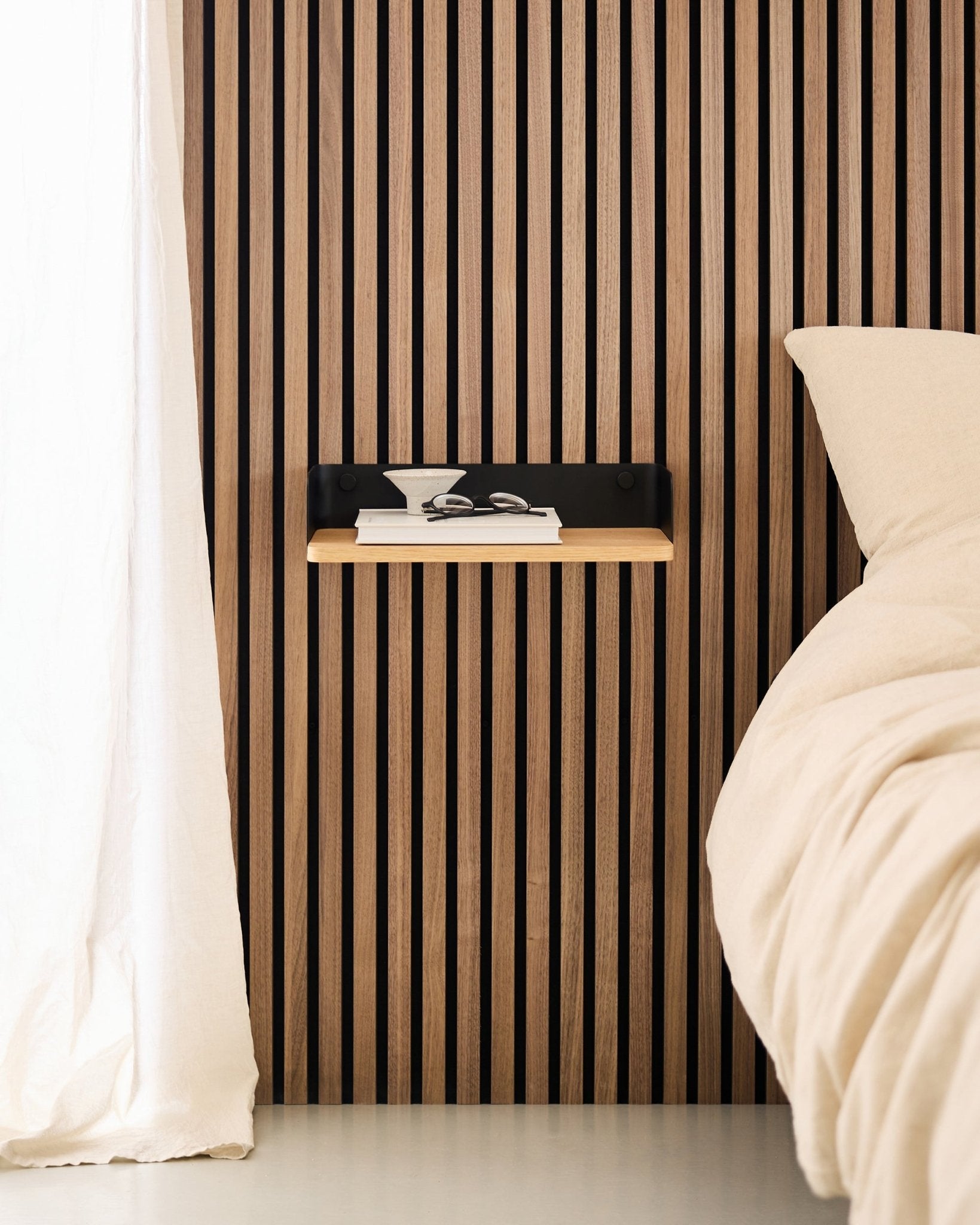 Minimalistiskt sovrum med en nordisk vägg med trälameller Akustikpanel, WoodUpp Linn bokhylla i Natural Oak och ett svävande nattduksbord bredvid en beige säng.