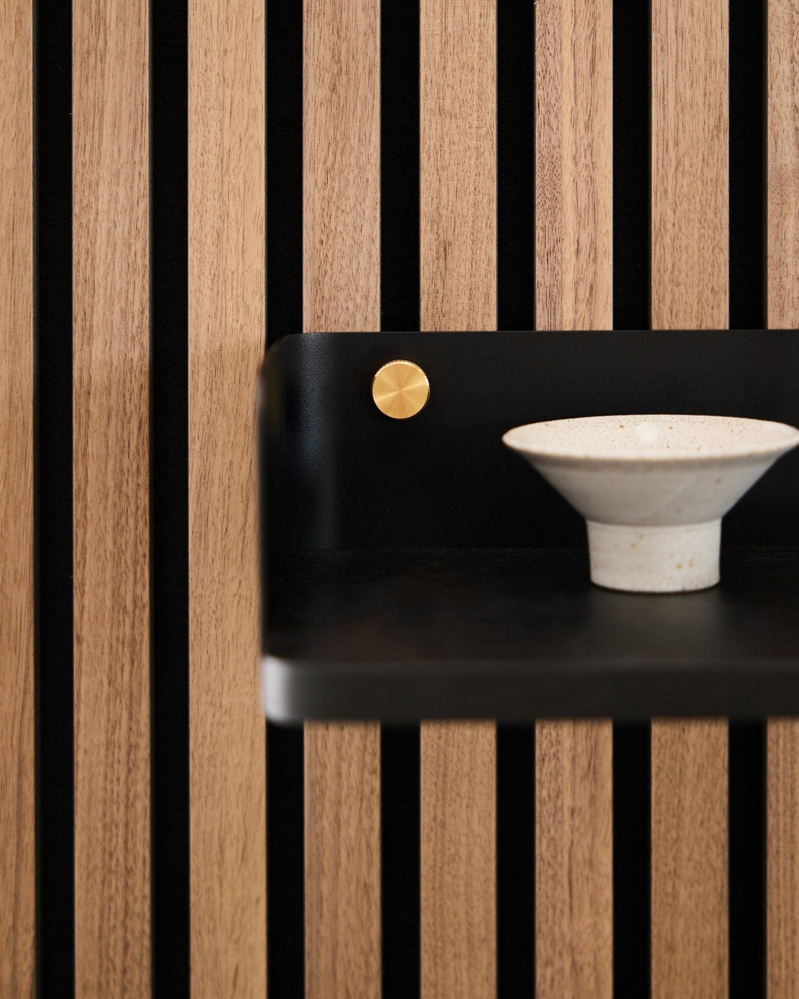 Keramisk skål placerad på Linn Bookshelf från WoodUpp, 39,9 cm i black oak med vertical black ribbor och en brass accent, som speglar nordisk minimalistisk design.