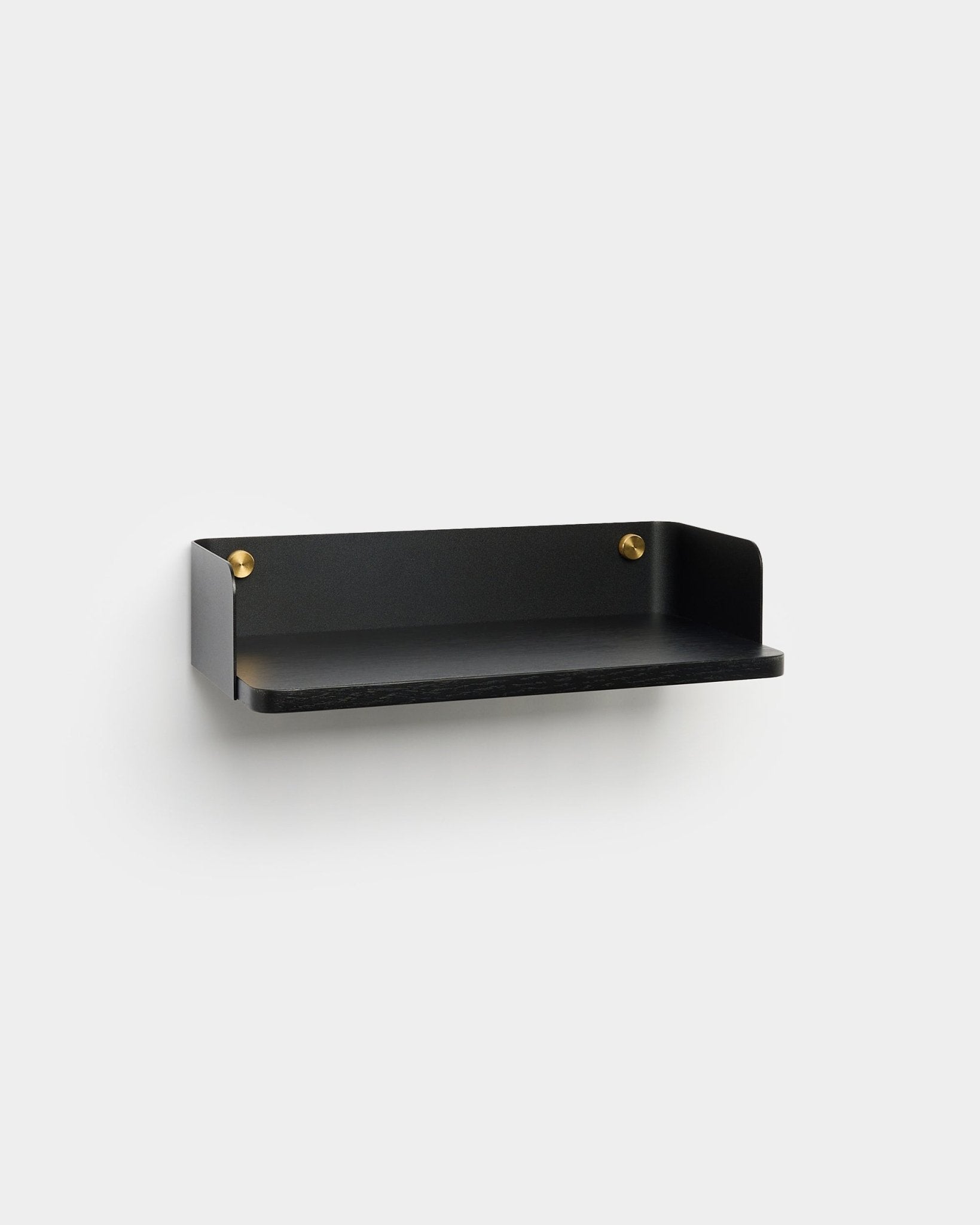 Linn Bokhylla från WoodUpp, i en minimalistisk black finish med brass monteringsskruvar, är monterad på en ljusgrå vägg och kompletterar nordisk inredningsdesign.