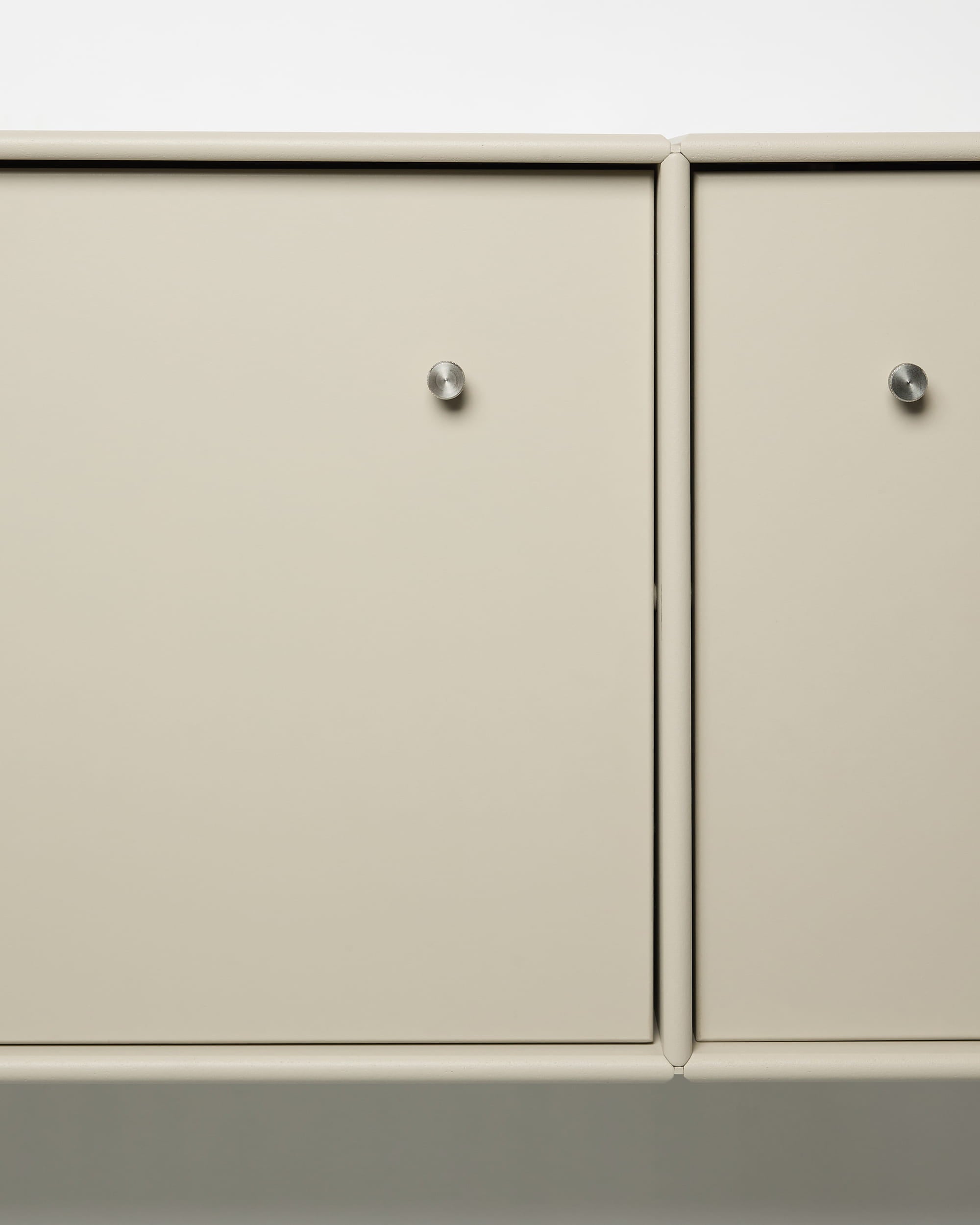 TV-bänken Arka från WoodUpp med beige skåpdörrar i metall, runda silverknoppar, modulär design och integrerad kabelhantering – perfekt för nordiska inredningar.