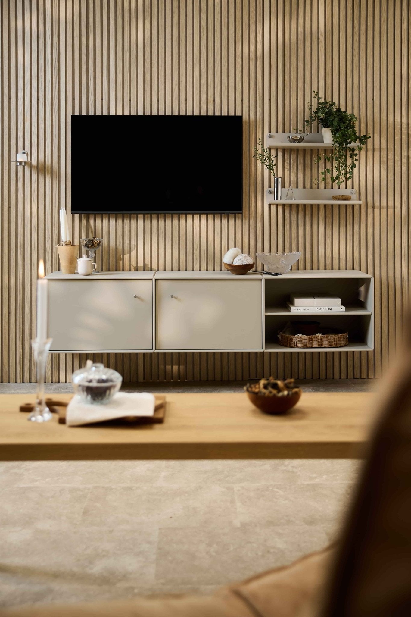 Ett modernt vardagsrum med TV-bänken Arka från WoodUpp, modulära sittmöbler, nordiska hyllor med växter och inredningsdetaljer samt ett ljus på soffbordet.
