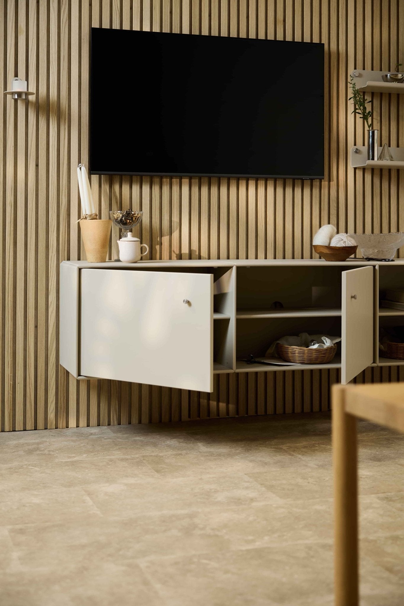 Ett modernt vardagsrum med TV-bänken Arka i beige från WoodUpp placerad under ett skåp och en TV på en akustisk trälamellvägg av typen Akupanel i nordisk stil. Modulmöbler.
