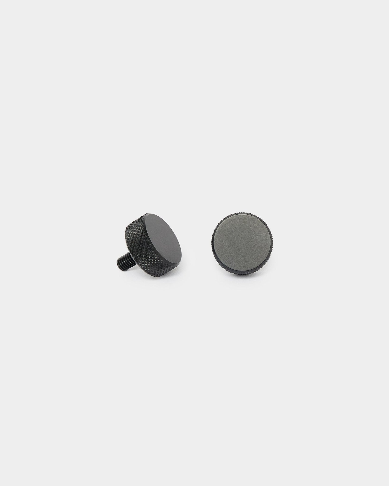 Två black WoodUpp Finger-skruvar (2 st, M5x10 mm, 20x8.8) visas stående och liggande på en vit bakgrund för montering av Akupanel.