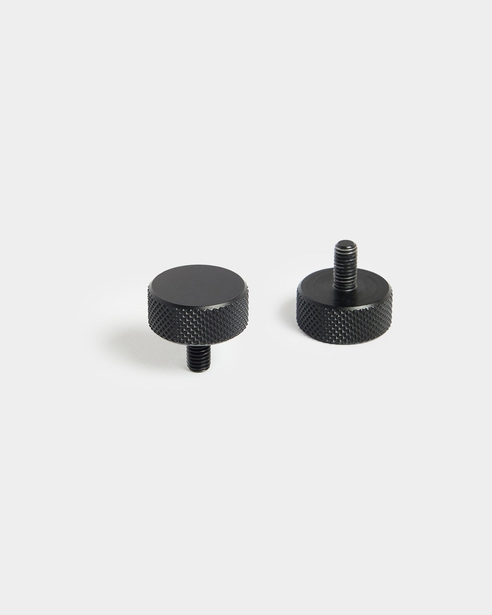 Ett par black WoodUpp Finger-skruvar (M5x10 mm, 20x8,8) med räfflade kanter, utformade för användning med Akustikpanel tillbehör, på vit bakgrund.
