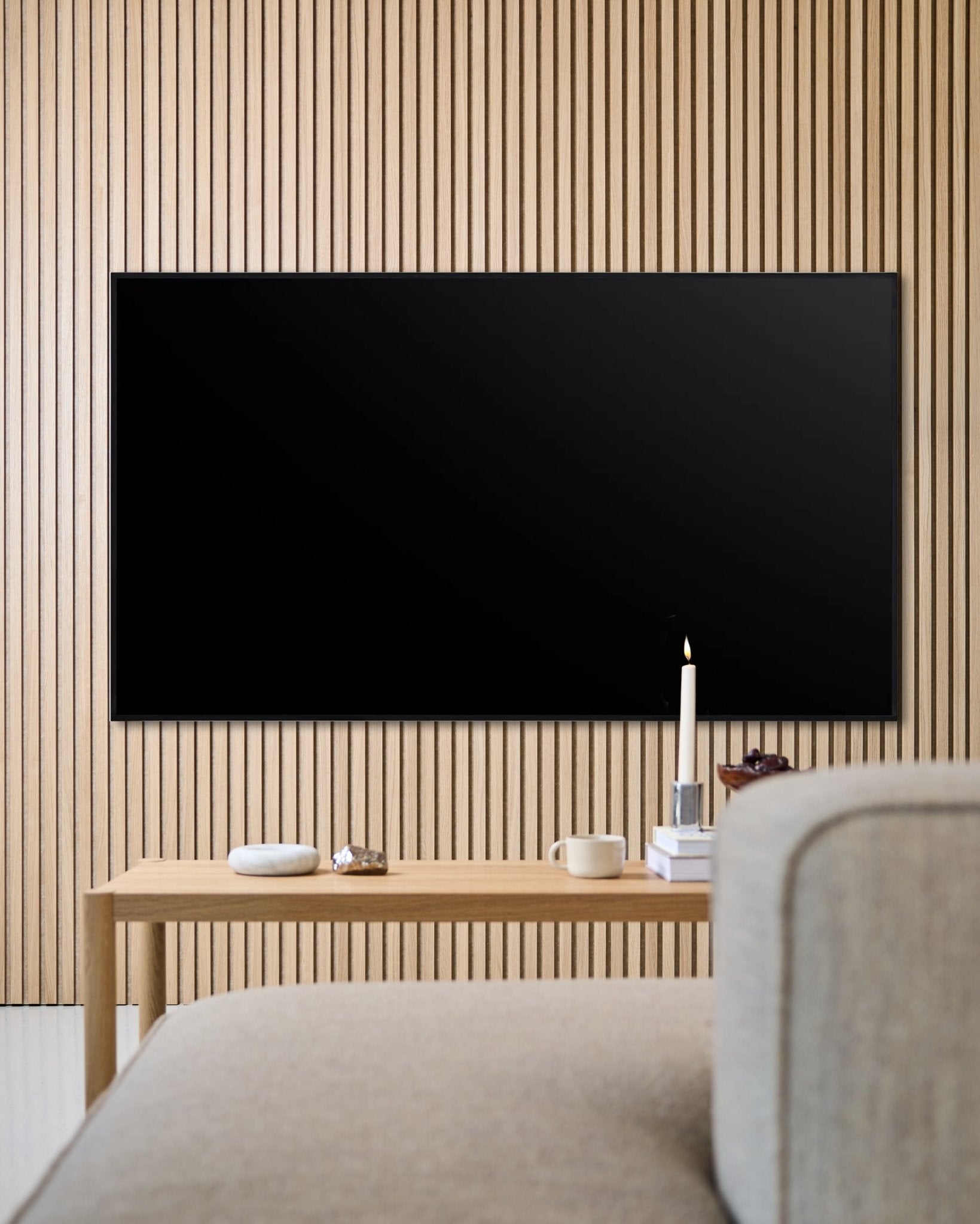 Modernt vardagsrum med en väggmonterad platt-TV, Akupanel vägg med akustiska trälameller och ett soffbord i trä som skapar en ombonad känsla.