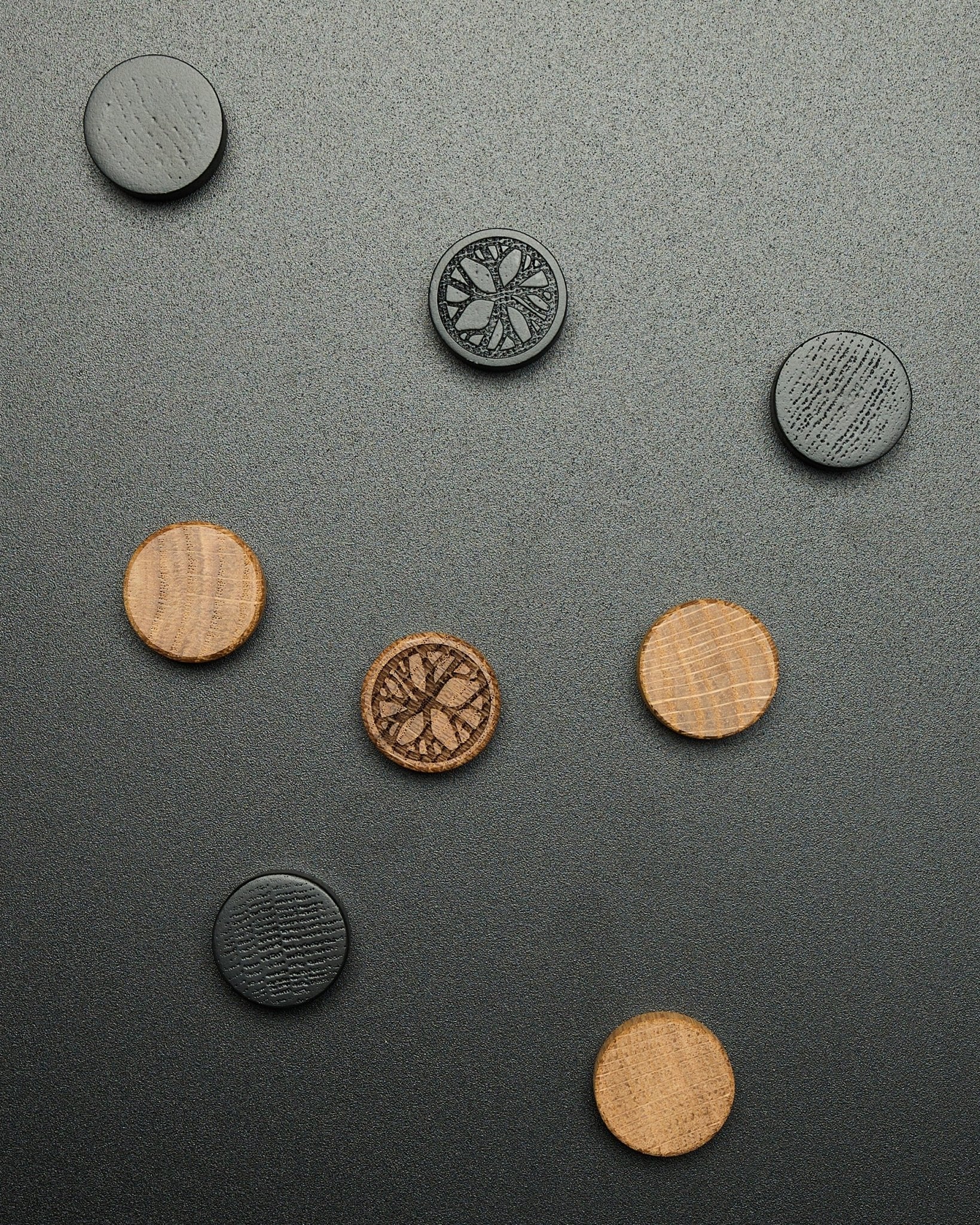 Fyra runda black oak magneter från WoodUpp Norr Magnet Set, löst placerade på en texturerad mörk yta, utformade som Akupanel tillbehör.