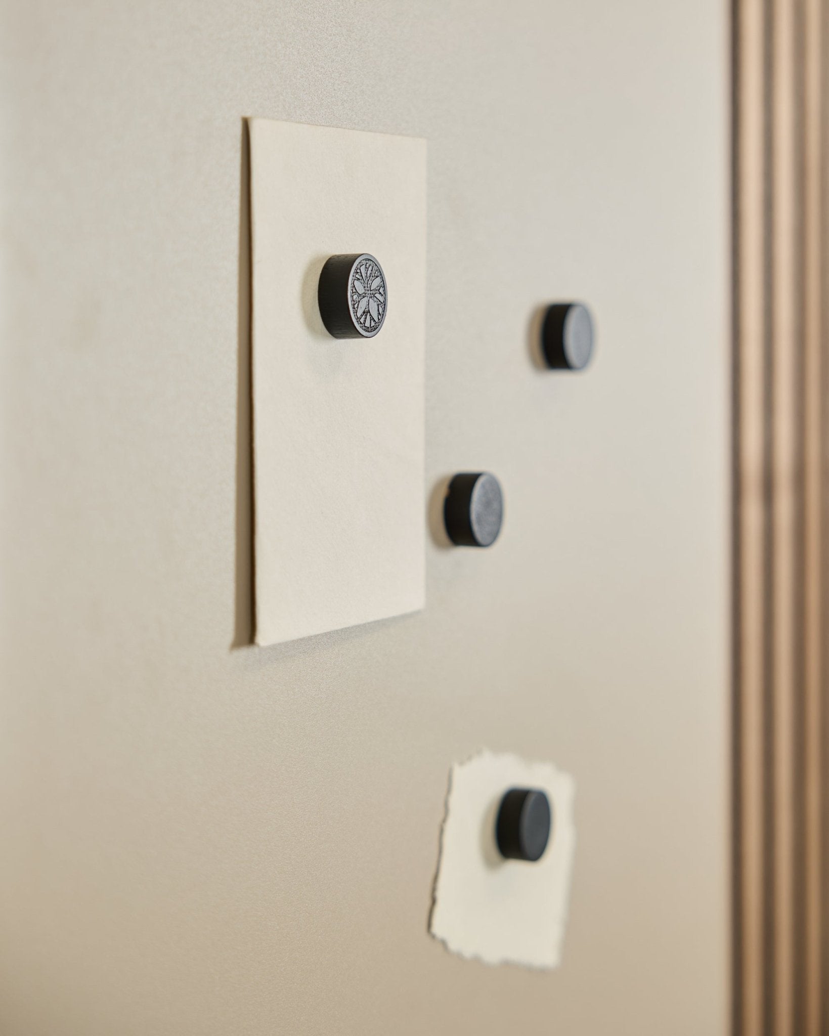 Fyra WoodUpp Norr Magnet set i Black Oak (4 st) håller fast två papper på en Norr Magnetic Board, med en del av en Akustikpanel synlig till höger.