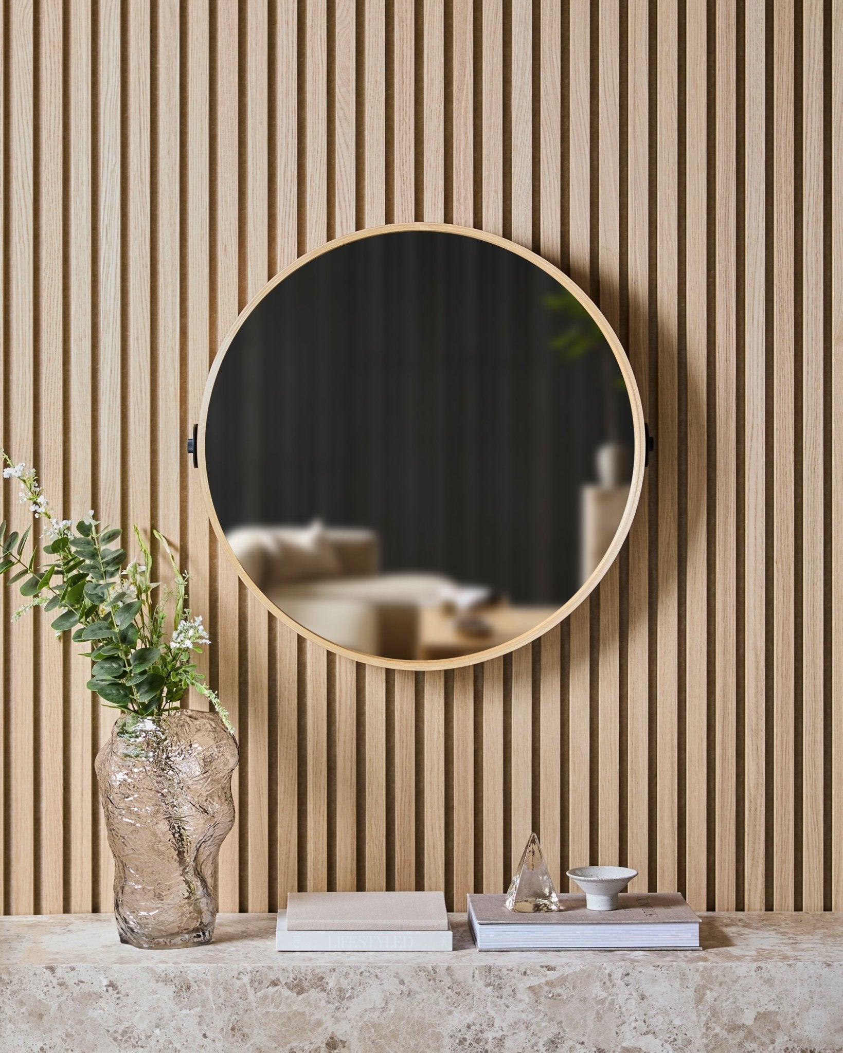 Linn | Mirror i Natural Oak från WoodUpp är monterad på en nordisk slatwall Akustikpanel ovanför en stenhylla med en glasvas, böcker och inredningsdetaljer.