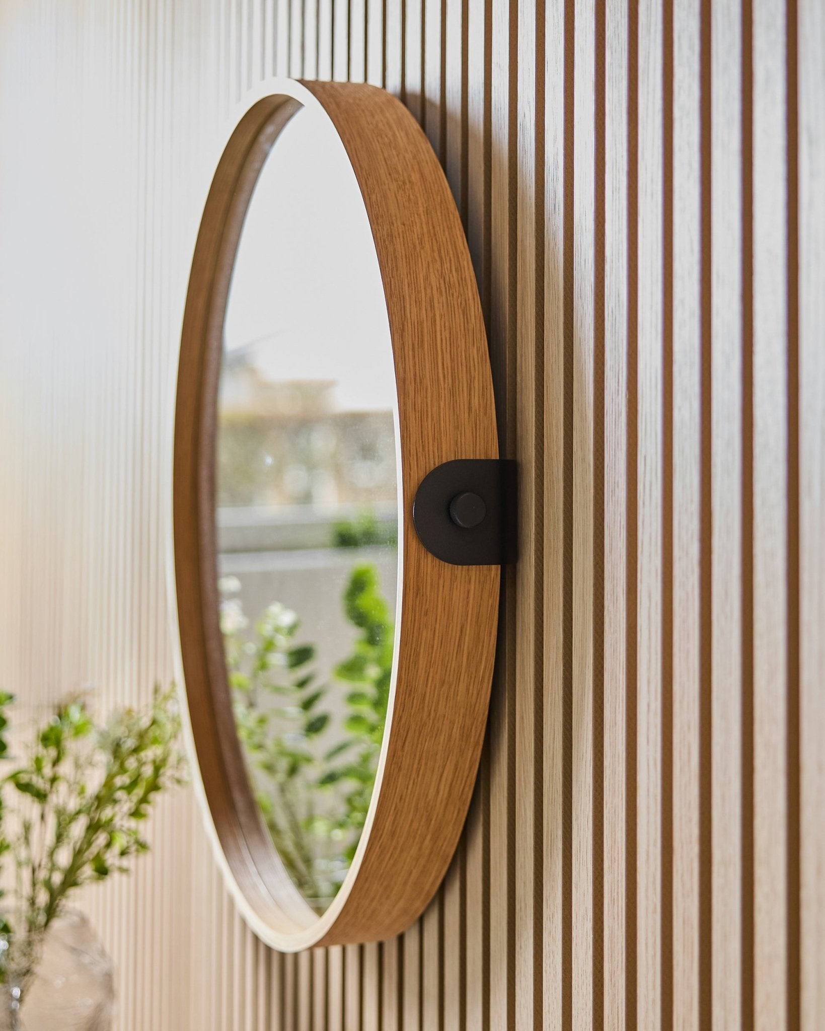 Linn | Mirror / Natural Oak från WoodUpp monterad på en randig vägg i Akustikpanel, som speglar grönska och naturligt ljus från ett närliggande fönster.