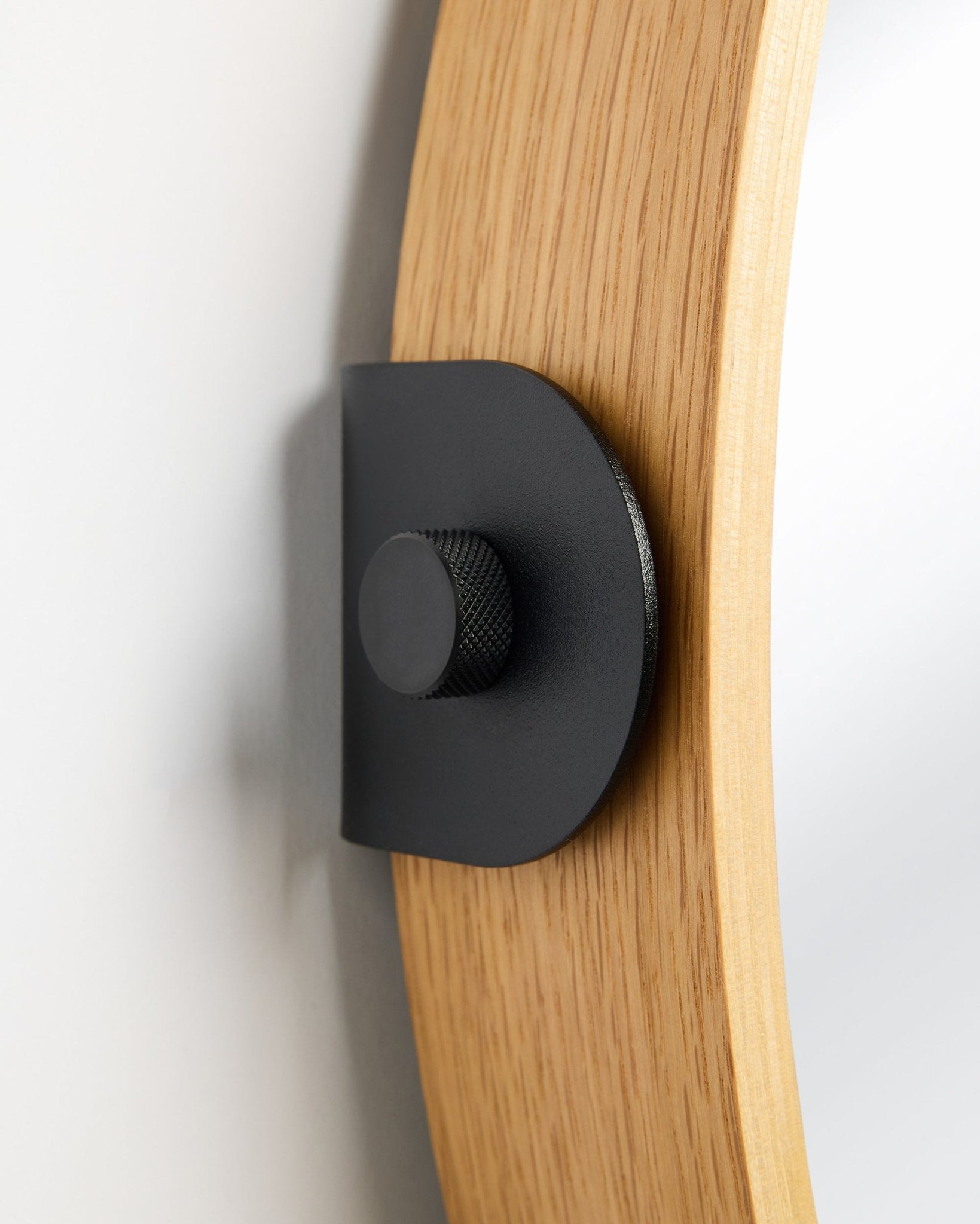 Detalj av WoodUpp Linn Mirror i Natural Oak, en Akustikpanel monterad på väggen med ett metallfäste i black och en rund knopp.