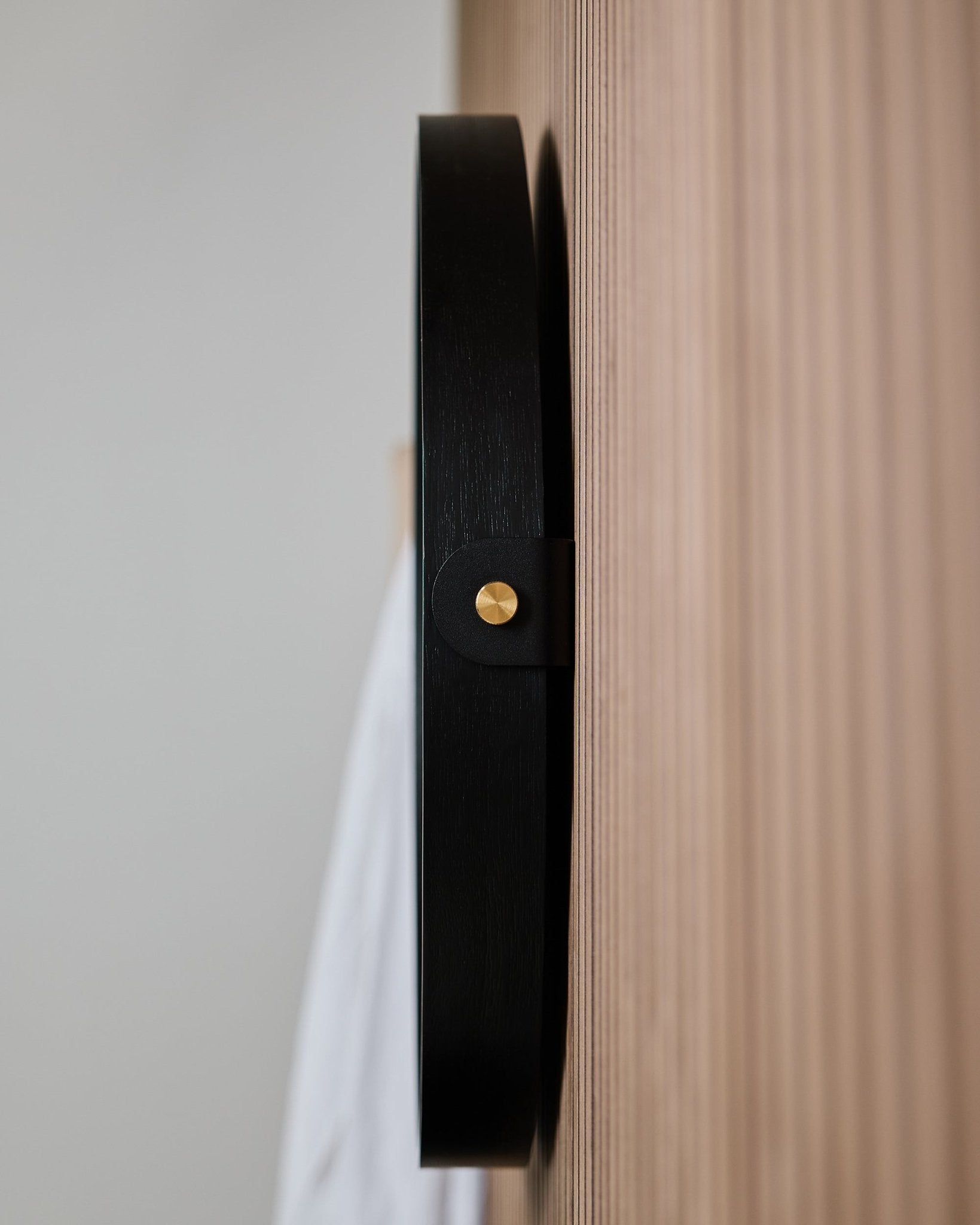 Närbild från sidan av väggkroken WoodUpp Linn | Mirror / Black Oak, monterad på en räfflad ekAkustikpanel, utformad för att hänga en rund spegel.