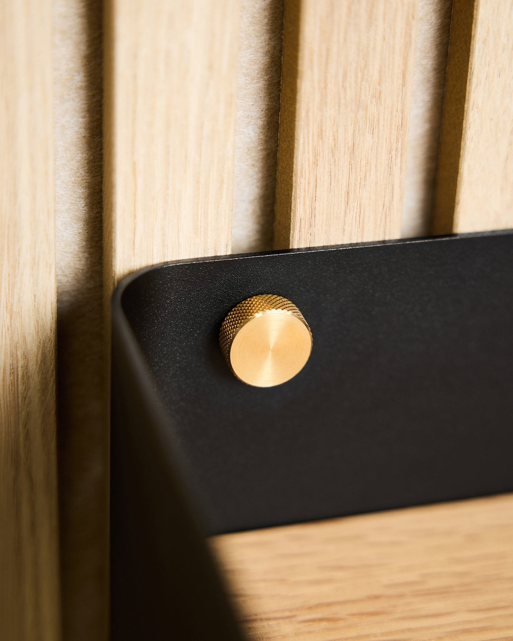 Närbild av två brass WoodUpp fingerskruvar (M5x10mm, 20x8.8), fästa på ett black beslag monterat på en ljus nordisk träyta Akustikpanel.