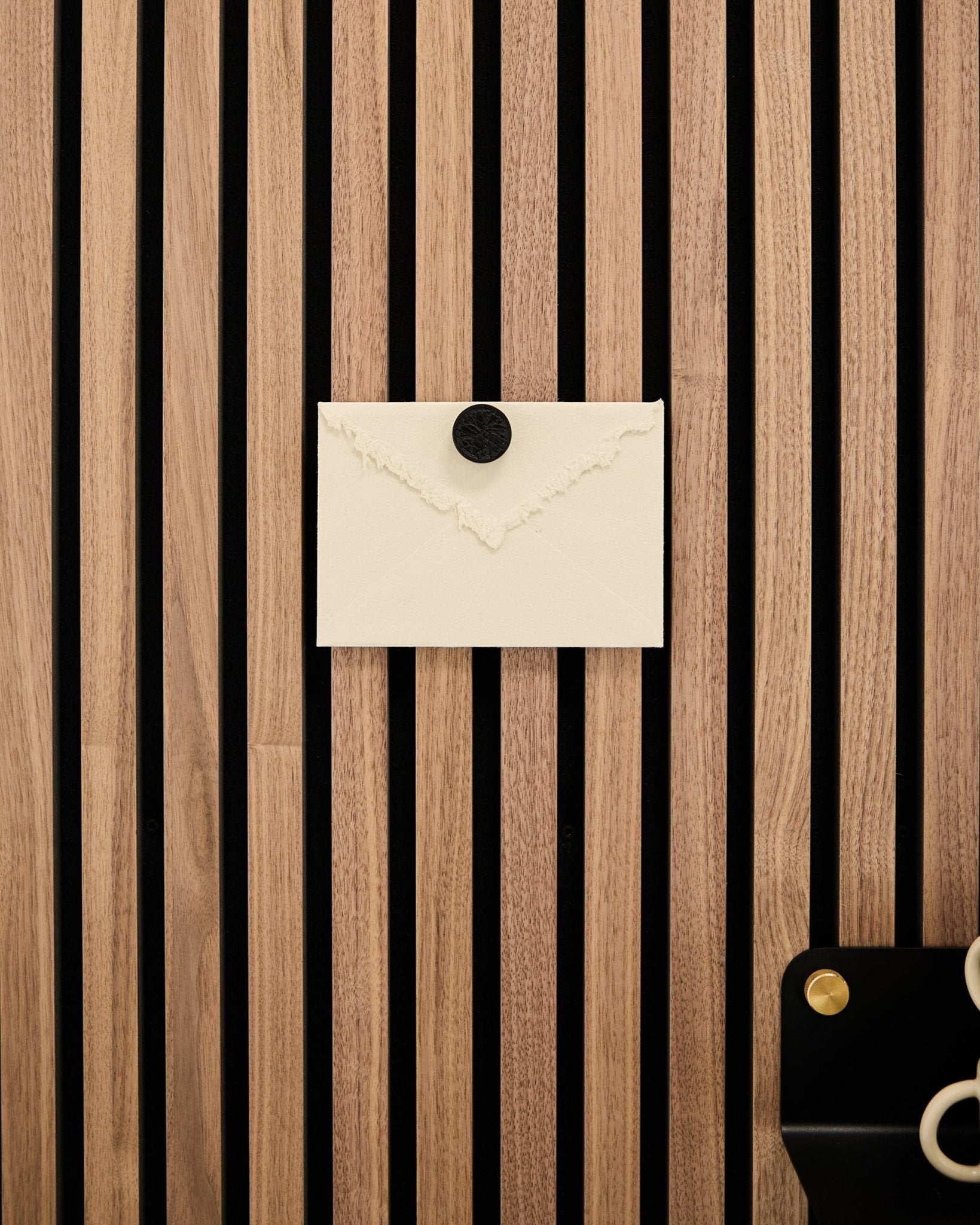 Ett krämfärgat kuvert är fäst på en WoodUpp Akupanel ekrandig Akustikpanel med hjälp av Norr Poster Magnet-setet i Black Oak; en sax ligger längst ner till höger.