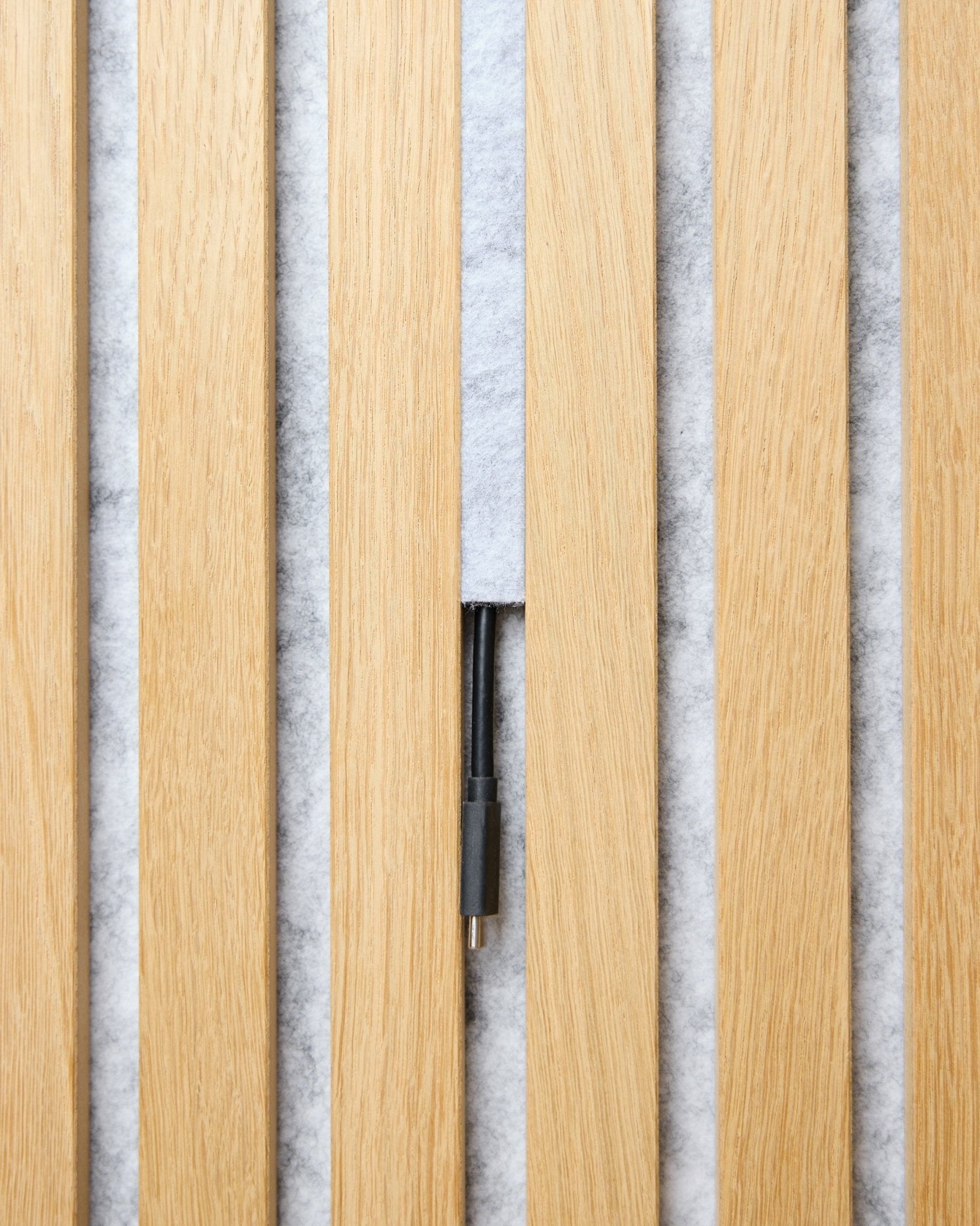 Dupps Pop-on Cable Cover-set (grey, 3 st) från WoodUpp organiserar kablar mellan ljusa Akupanel träribbor mot en vit texturerad bakgrund.