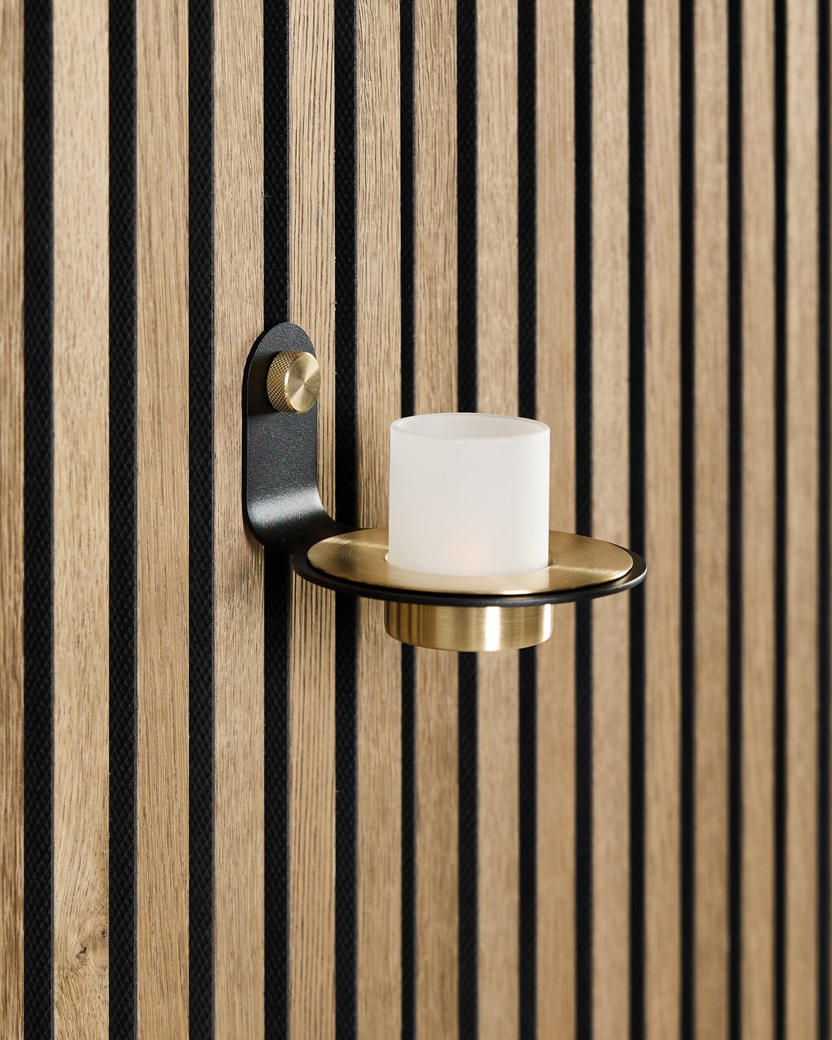 Norr ljushållare i black och brass från WoodUpp är monterad på en nordisk Akupanel akustikpanel i trä med vertical ribbor i black.
