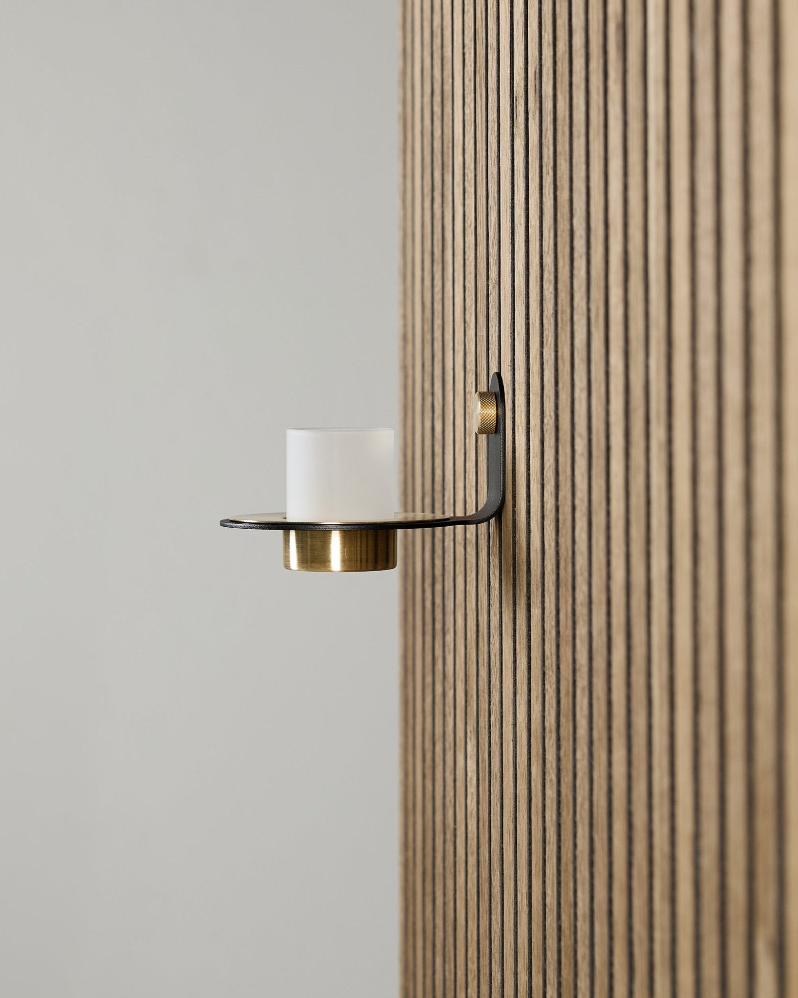 Norr ljushållare i black och brass från WoodUpp, monterad på en vertical Akupanel Akustikpanel, med frostat glas och detaljer i brass.
