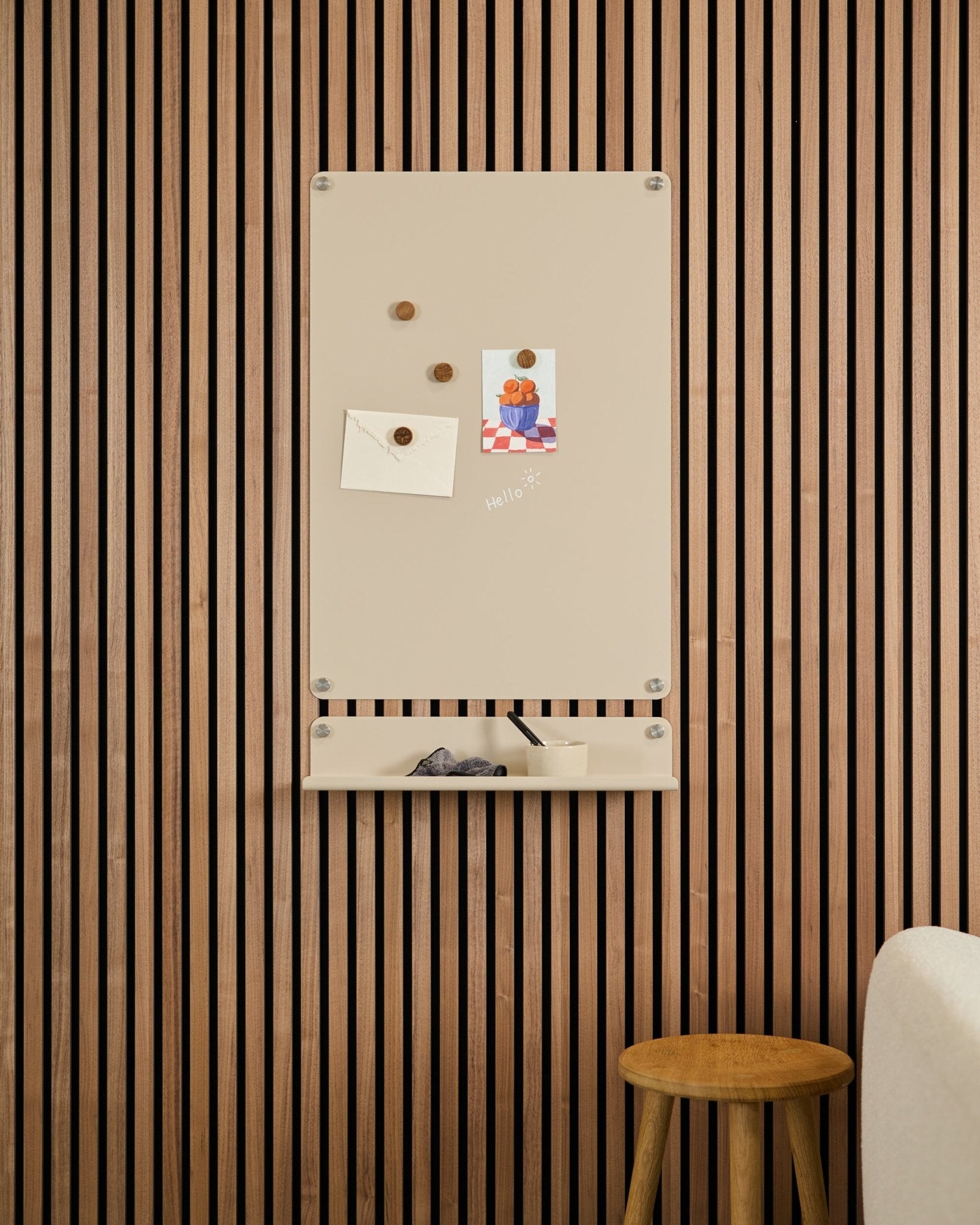 Beige Norr magnettavla från WoodUpp monterad ovanför en small hylla på en vägg med Akupanel akustikpanel i trä, med en pall och vit soffa i närheten.