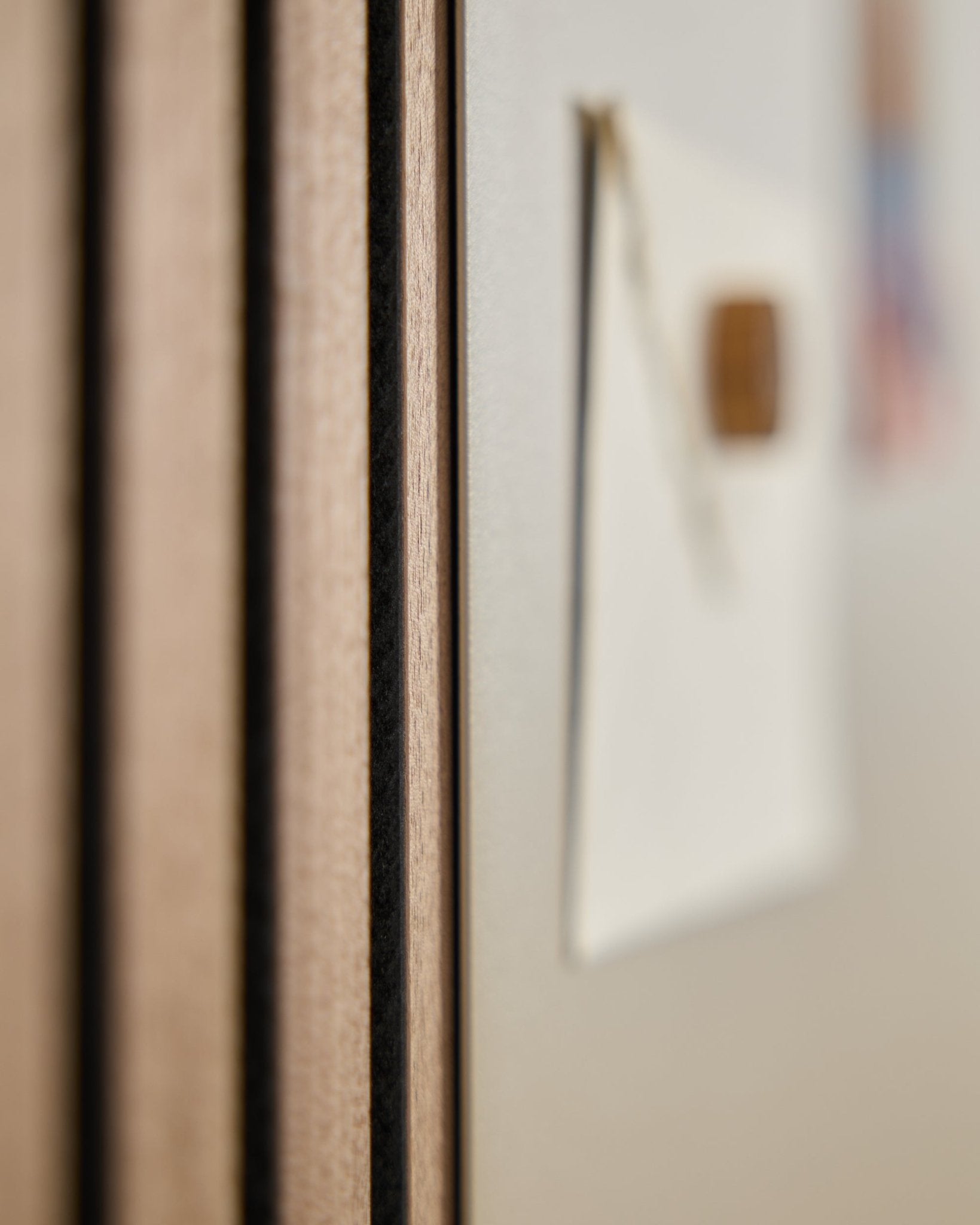 Närbild av en WoodUpp Akupanel akustikpanel i trä med vertical ribbor, bredvid en suddig large beige Norr magnettavla i bakgrunden.