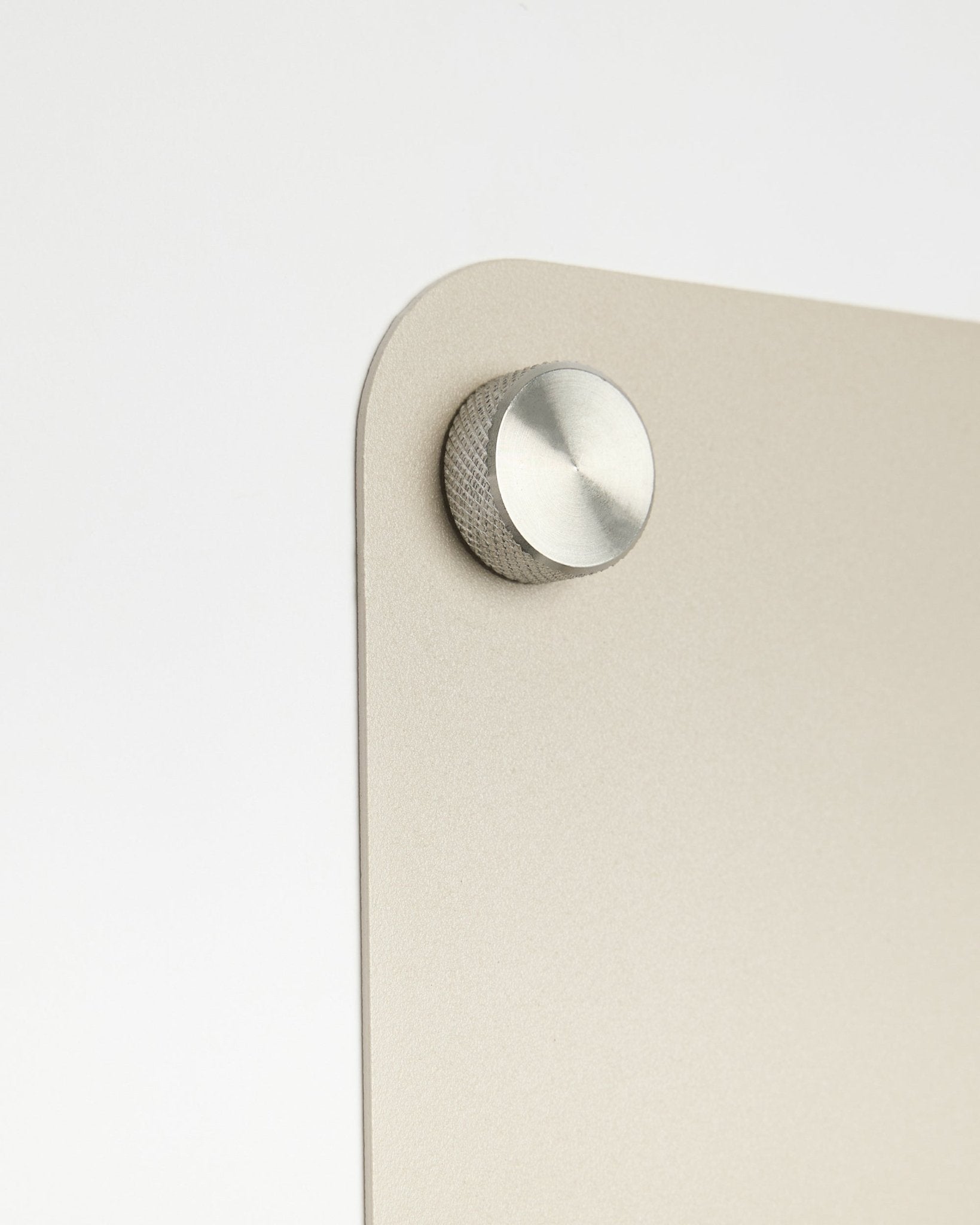 Närbild av en rund knopptillbehör i metall fäst på WoodUpps large beige Norr magnettavla, med detalj i frostat glas mot en vit bakgrund.