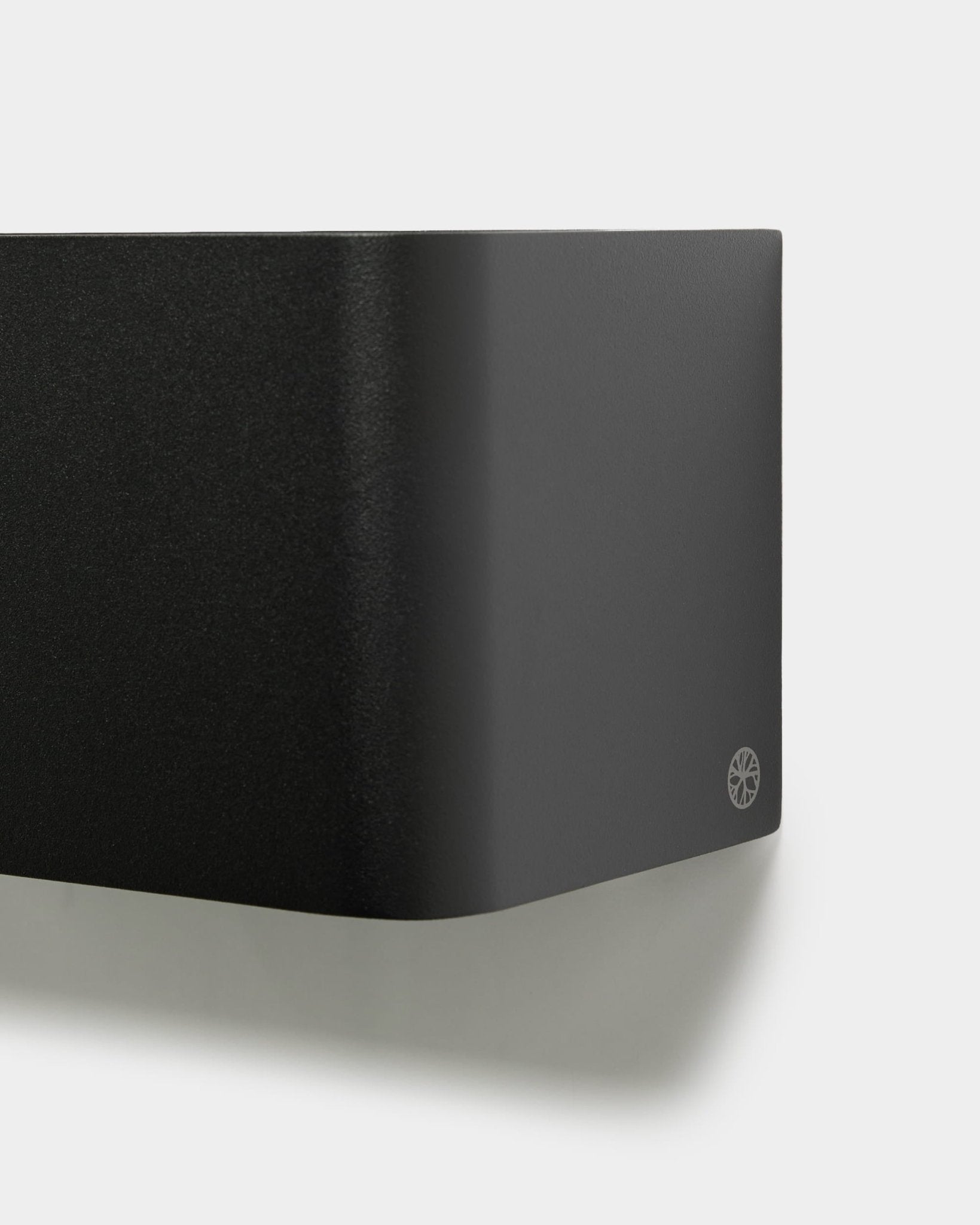 Närbild av den minimalistiska WoodUpp Norr Plant Box (23,9 cm, black) med rundade kanter och logotyp, monterad på en vit vägg. Nordisk design för akustiska tillbehör.