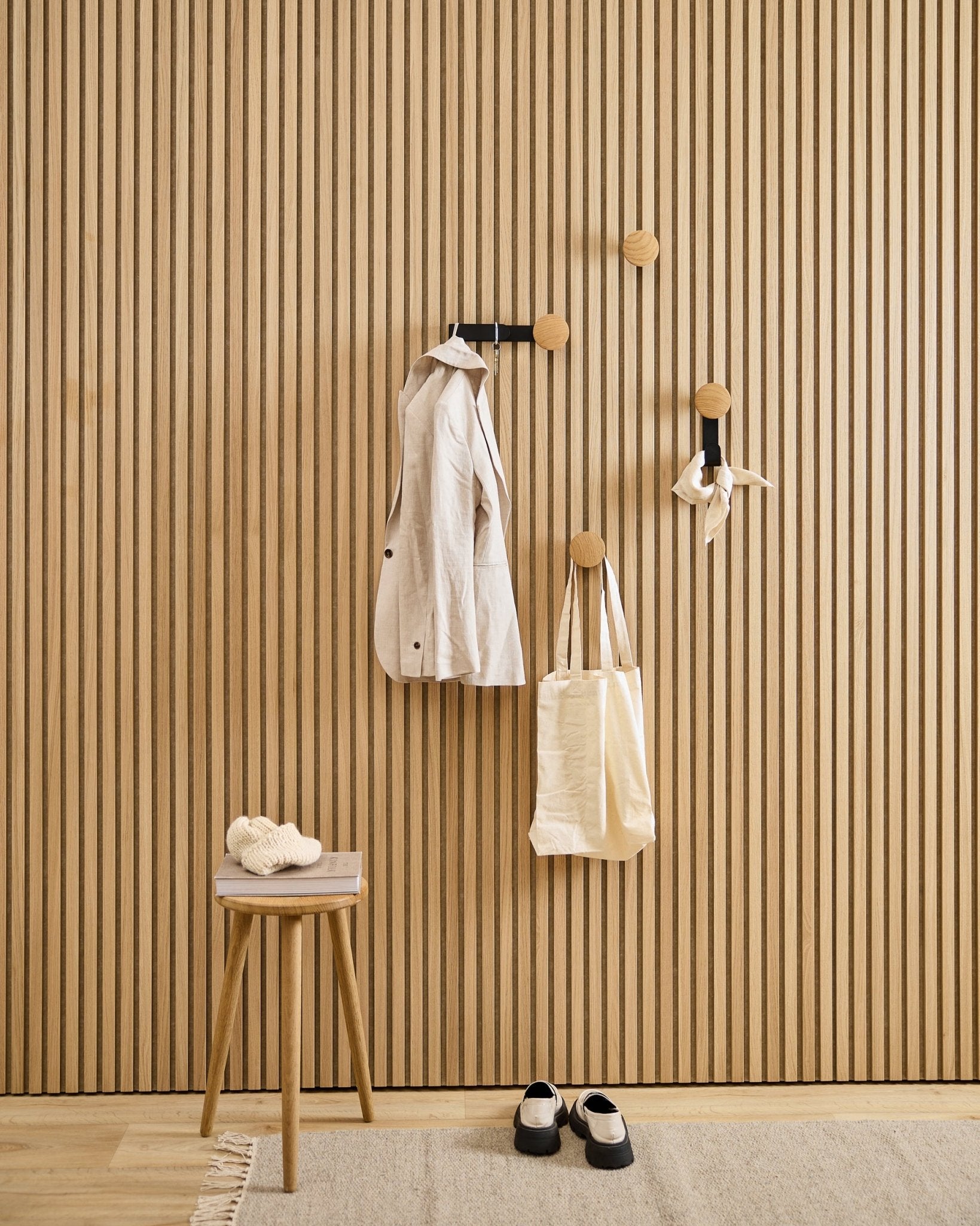 Minimalistisk hall med WoodUpp Linn Vertical Hanger i natural oak, med en beige kappa, tygväska, scarf, pall med tofflor och black-vita skor.