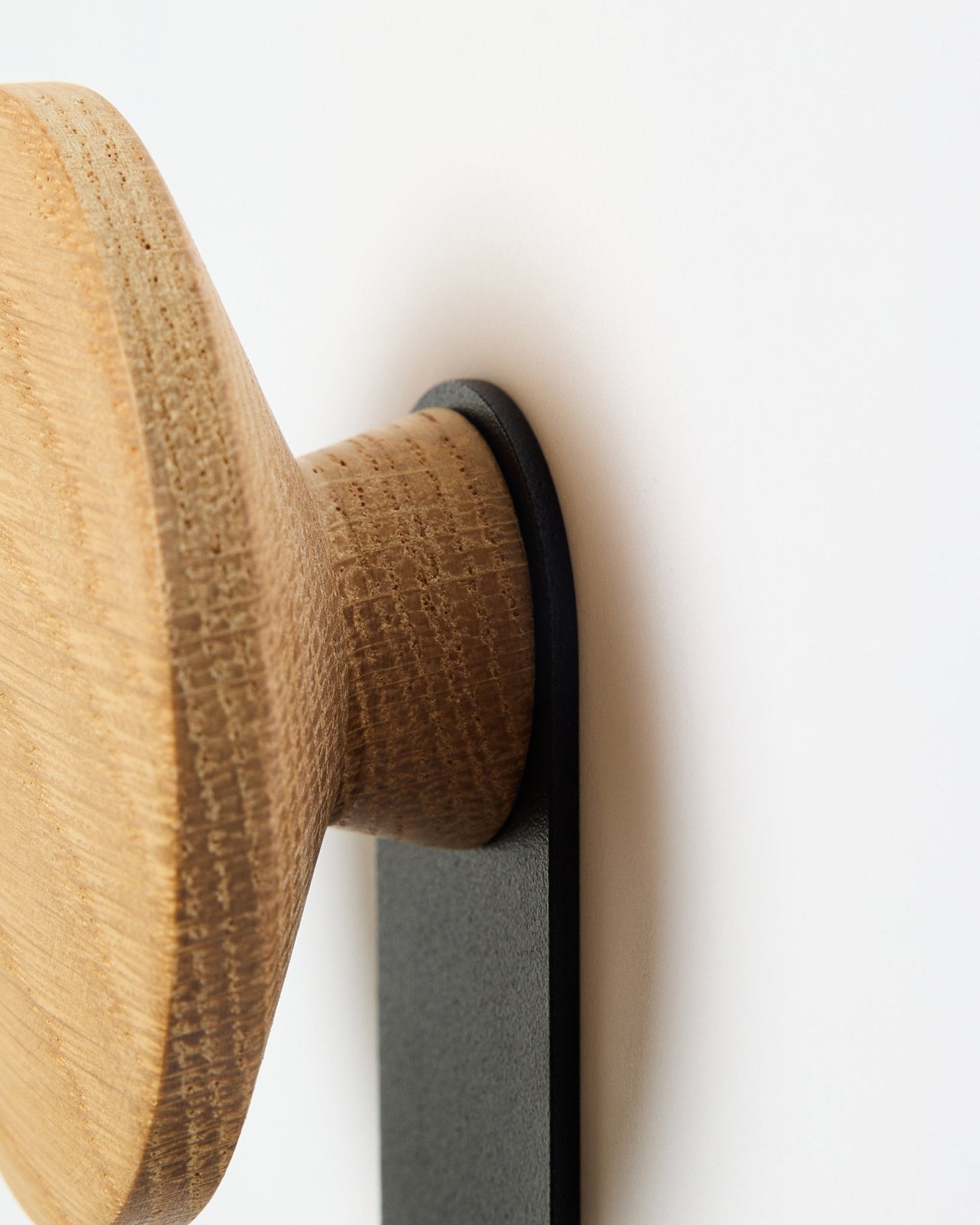 Närbild på Linn Vertical Hanger i natural oak från WoodUpp, en rund träknopp som är monterad på ett black fäste och utformad för Akupanel akustikpaneler.