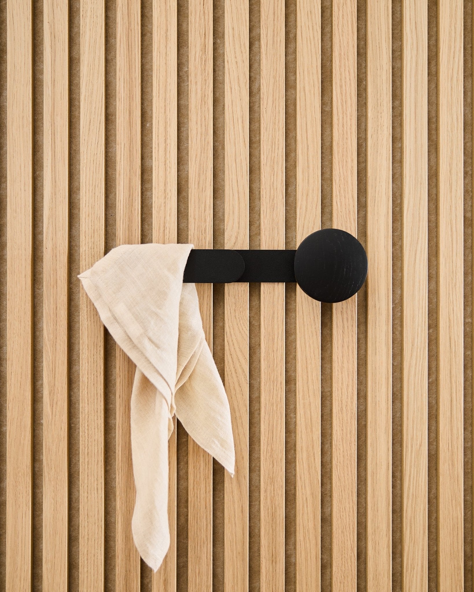 En beige duk hänger över WoodUpp Linn Horizontal Hanger i Black Oak, fäst på en vertical akustisk ribbpanel.