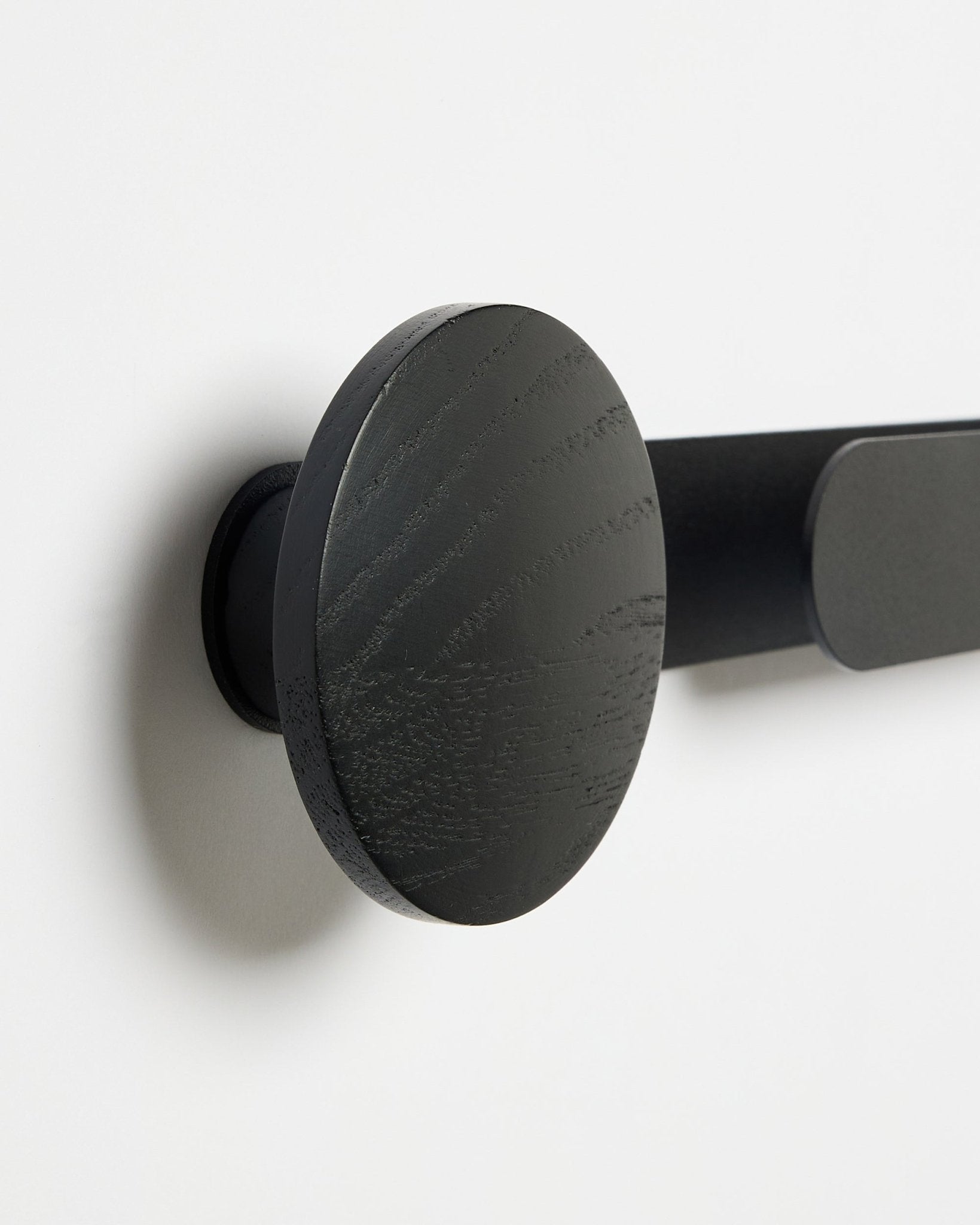 Närbild av WoodUpp Linn | Horizontal Hanger i Black Oak, matt black finish, monterad på en vit vägg; accessoar för akustiska träpaneler.