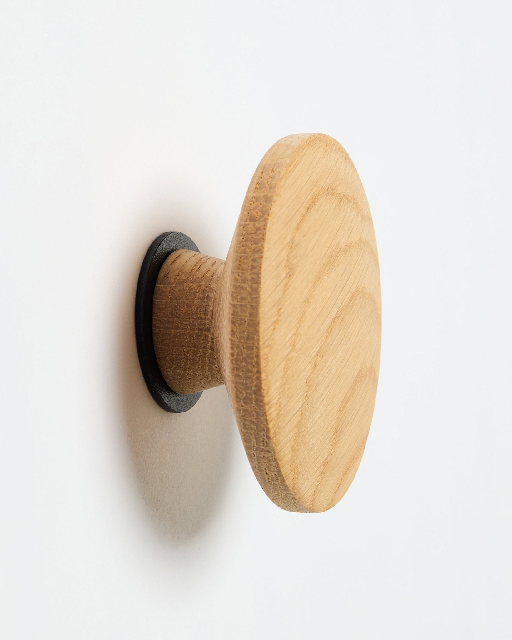 WoodUpp Linn I Single Hanger i natural oak, en rund väggkrok med black bas, designad som en accessoar för montering på Akupanel akustiska träpaneler.