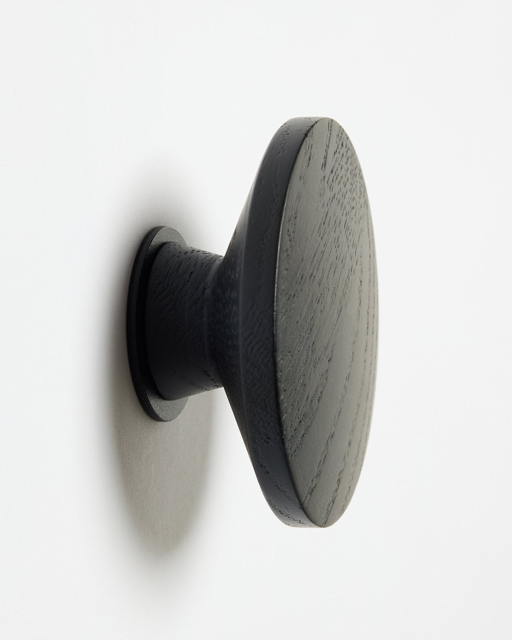 En rund Linn | Single Hanger från WoodUpp i black oak, utformad som en accessoar för Akupanel akustiska träpaneler, monterad på en vit yta med en mjuk skugga åt vänster.