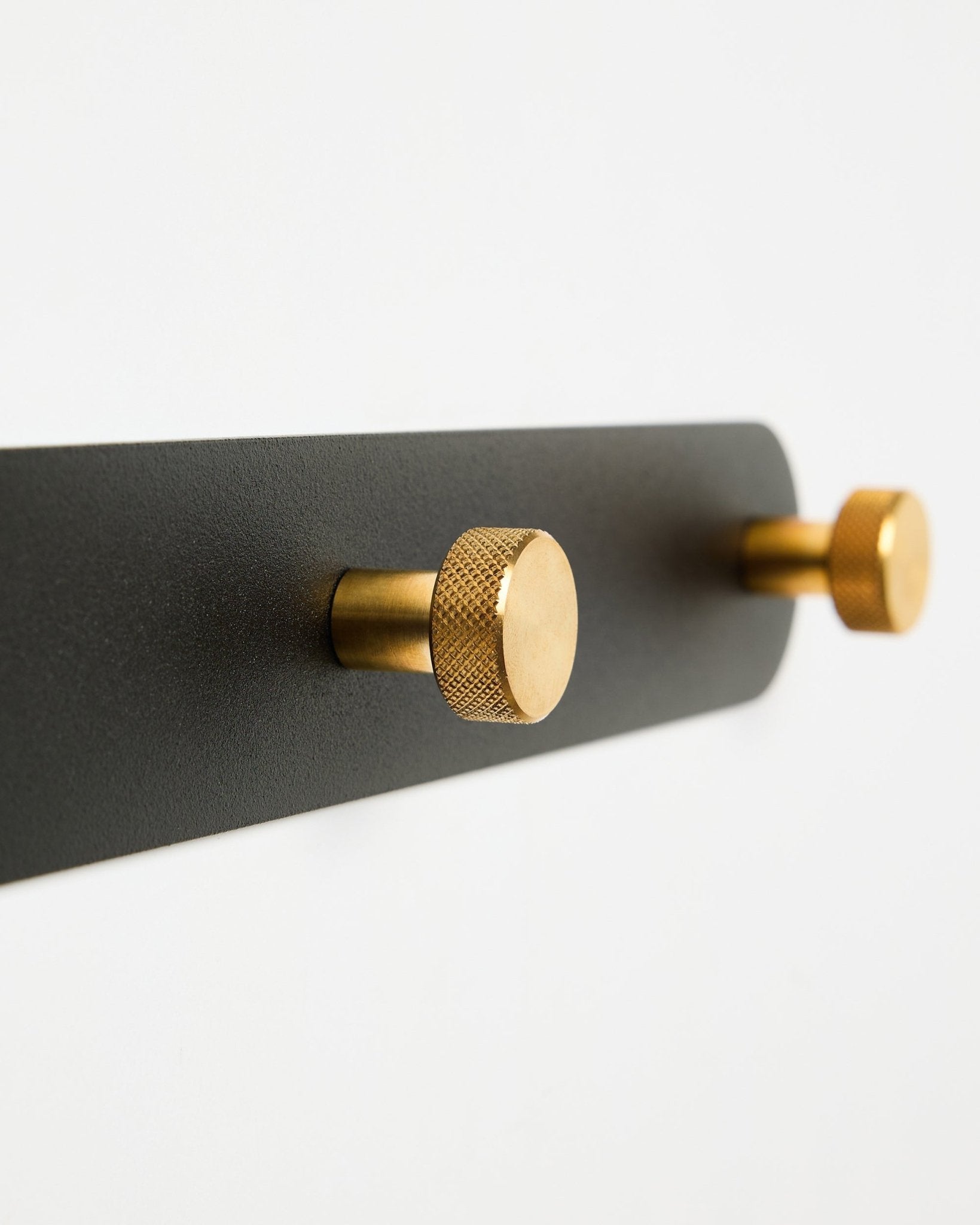 WoodUpp Norr Coat Hook Rack, modell X7, med två cylindriska black och brass krokar på ett black fäste, visad mot vit bakgrund.