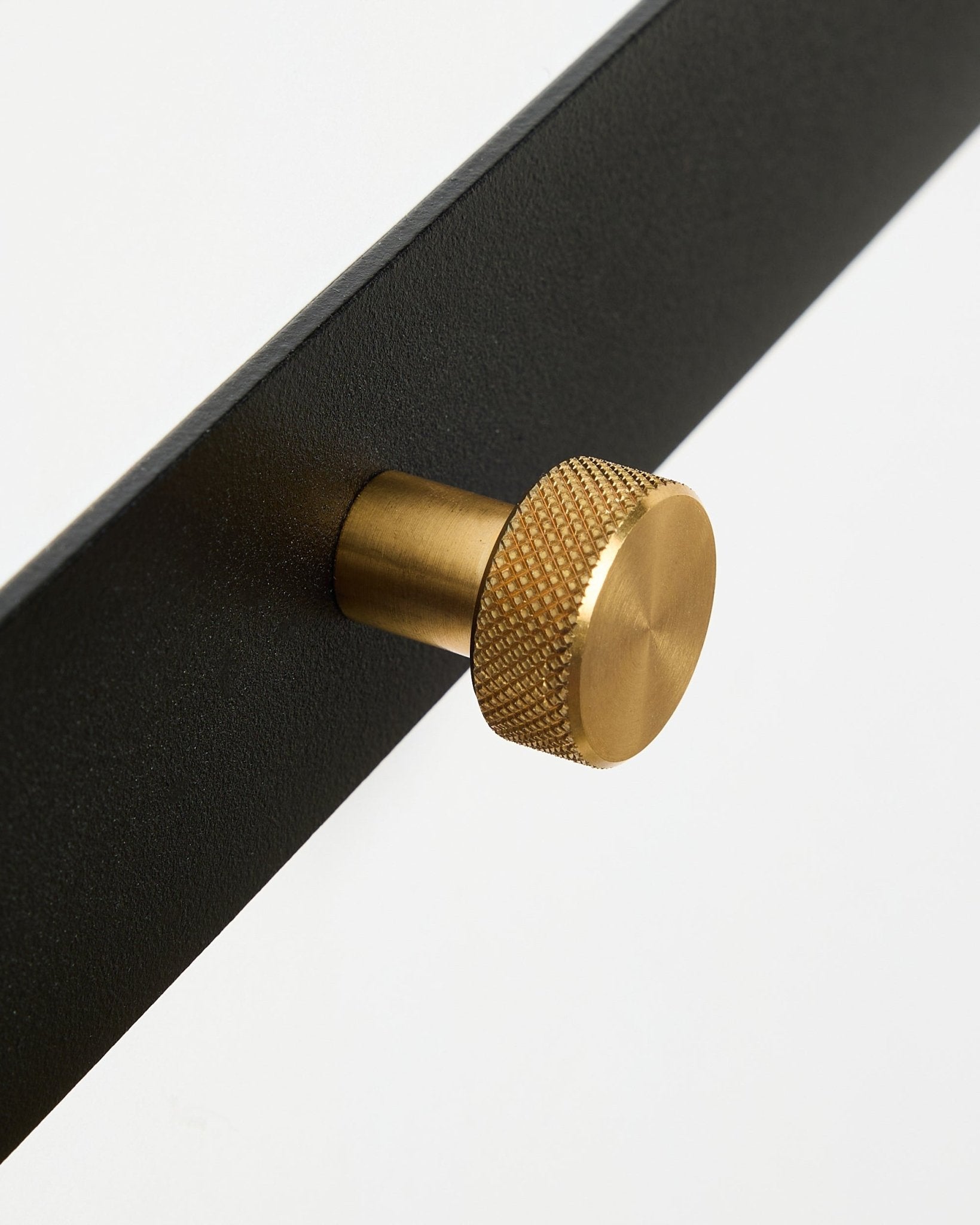 Närbild av Norr knopplist X5 från WoodUpp, med black pulverlackerad steel och runda, texturerade brass knoppar, mot en vit bakgrund.