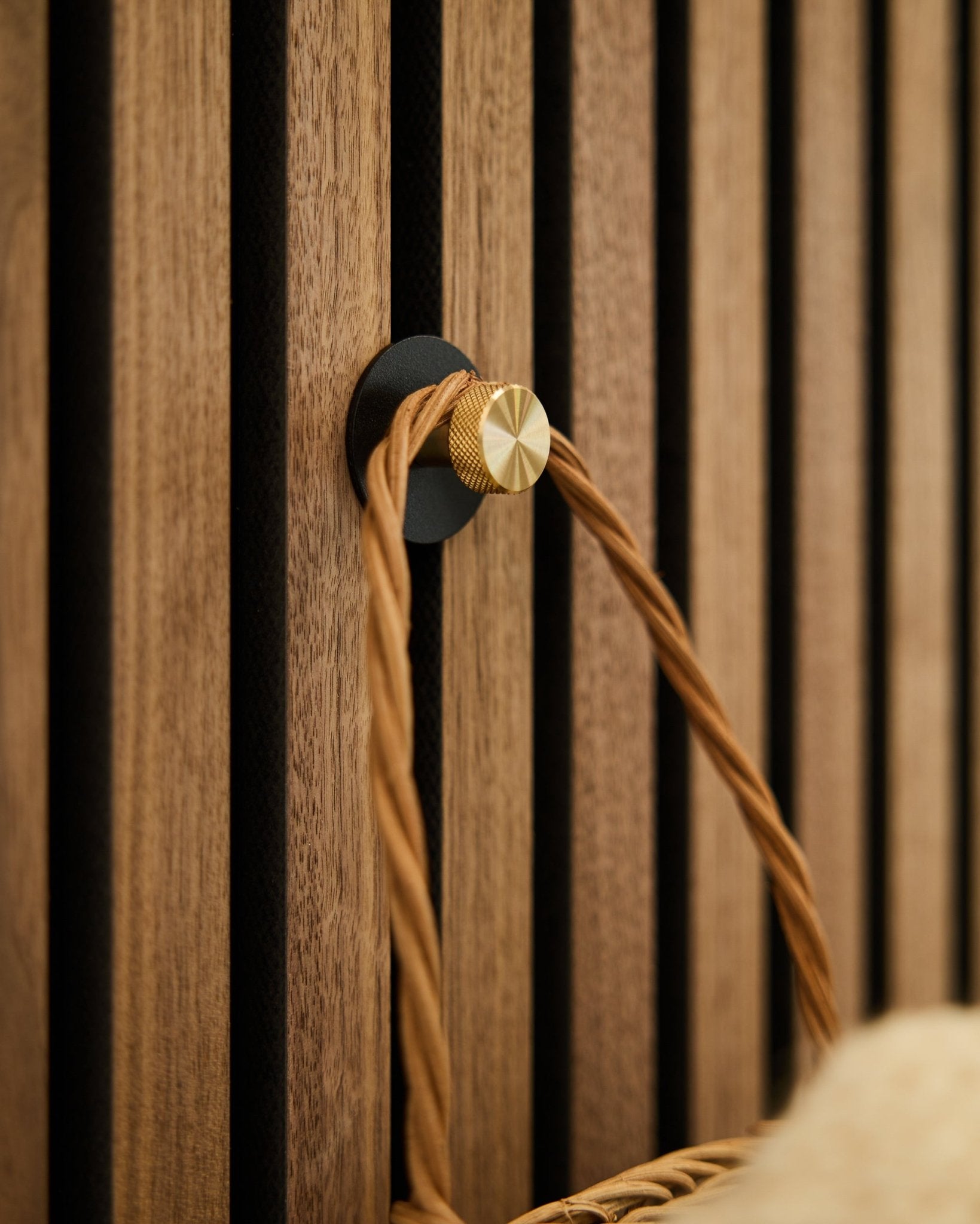 WoodUpp Norr klädkrok i black och brass, monterad på en träbas av Akupanel Akustikpanel, håller ett flätat handtag i tan.