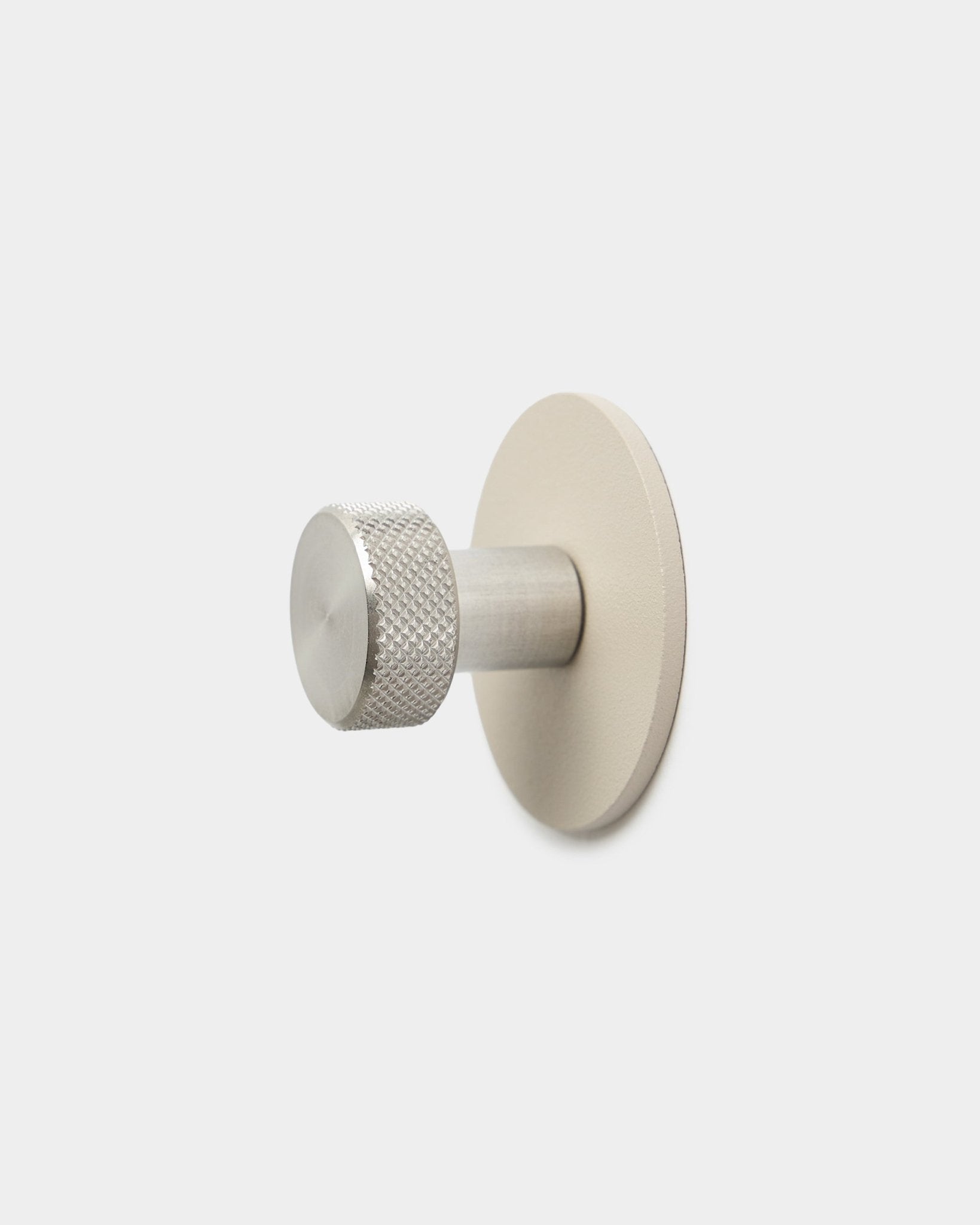 WoodUpp Norr Coat Hook i beige och rostfritt steel med en texturerad cylindrisk ände och rund bas, en accessoar för Akupanel, mot en enkel vit bakgrund.