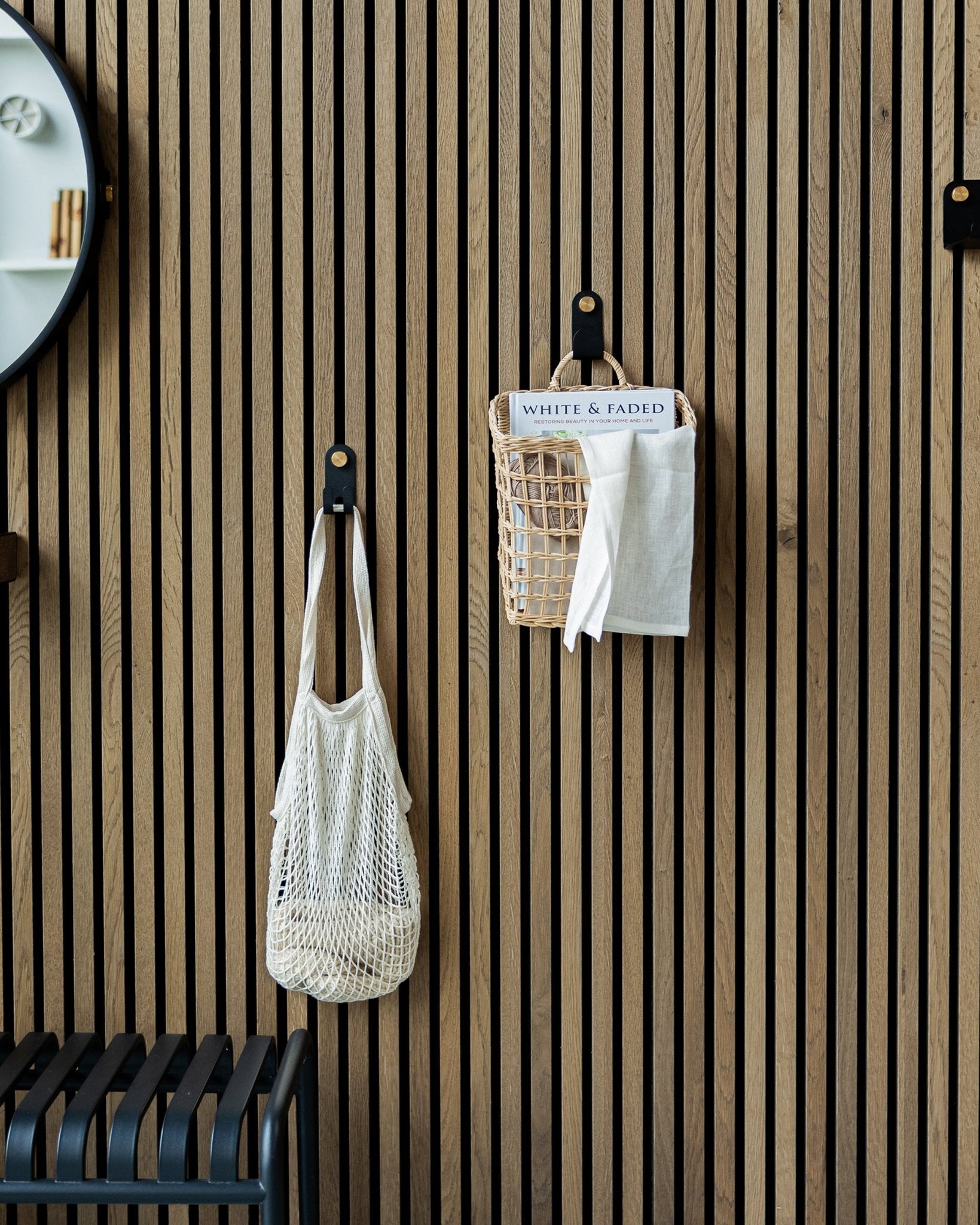 En nätväska och en korg hänger från Norr Single Hangers från WoodUpp på en nordisk trä-Akupanel Akustikpanel; en del av en spegel syns till vänster.