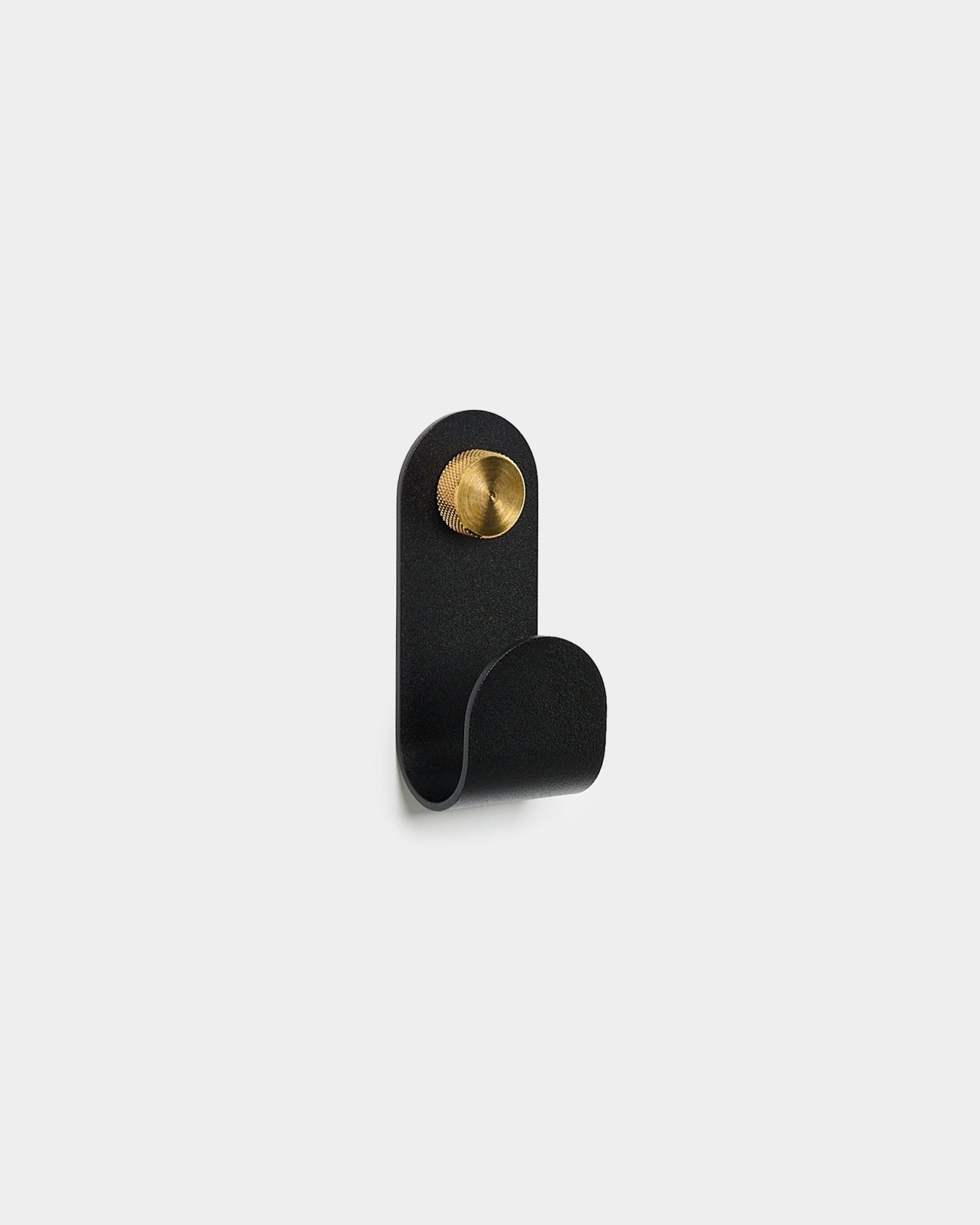 Norr Single Hanger i black från WoodUpp, med en böjd form och en rund brass detalj, visas mot en enkel vit bakgrund.