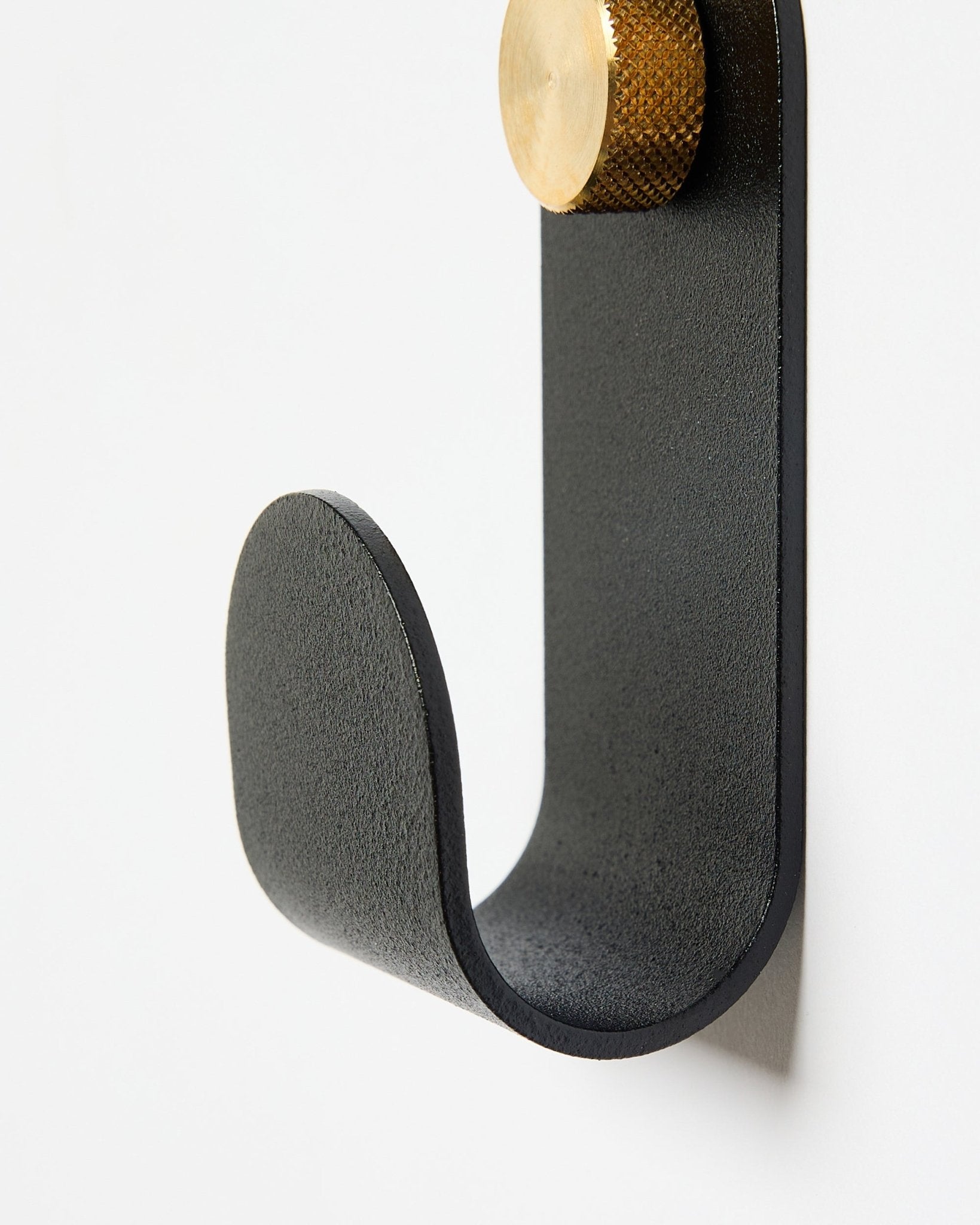 Norr Single Hanger från WoodUpp har en böjd metallarm i black med en guldfärgad topp, utformad som ett tillbehör för användning med akustikpaneler på vita väggar.