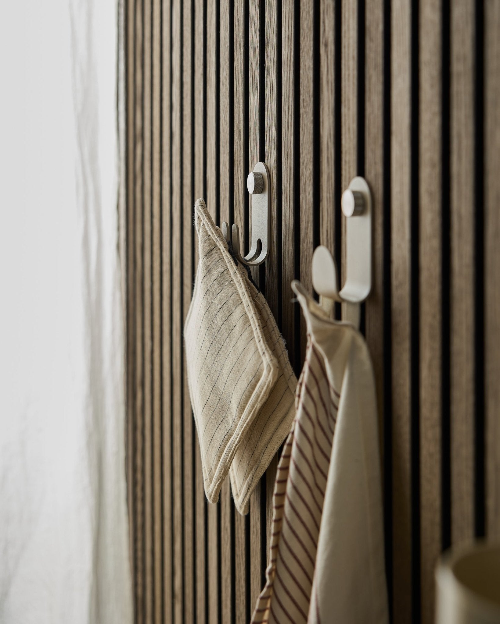 Två randiga kökshanddukar hänger på Norr Double Hanger från WoodUpp, monterad på en beige nordisk ribbväggspanel Akustikpanel, upplyst av mjukt naturligt ljus.